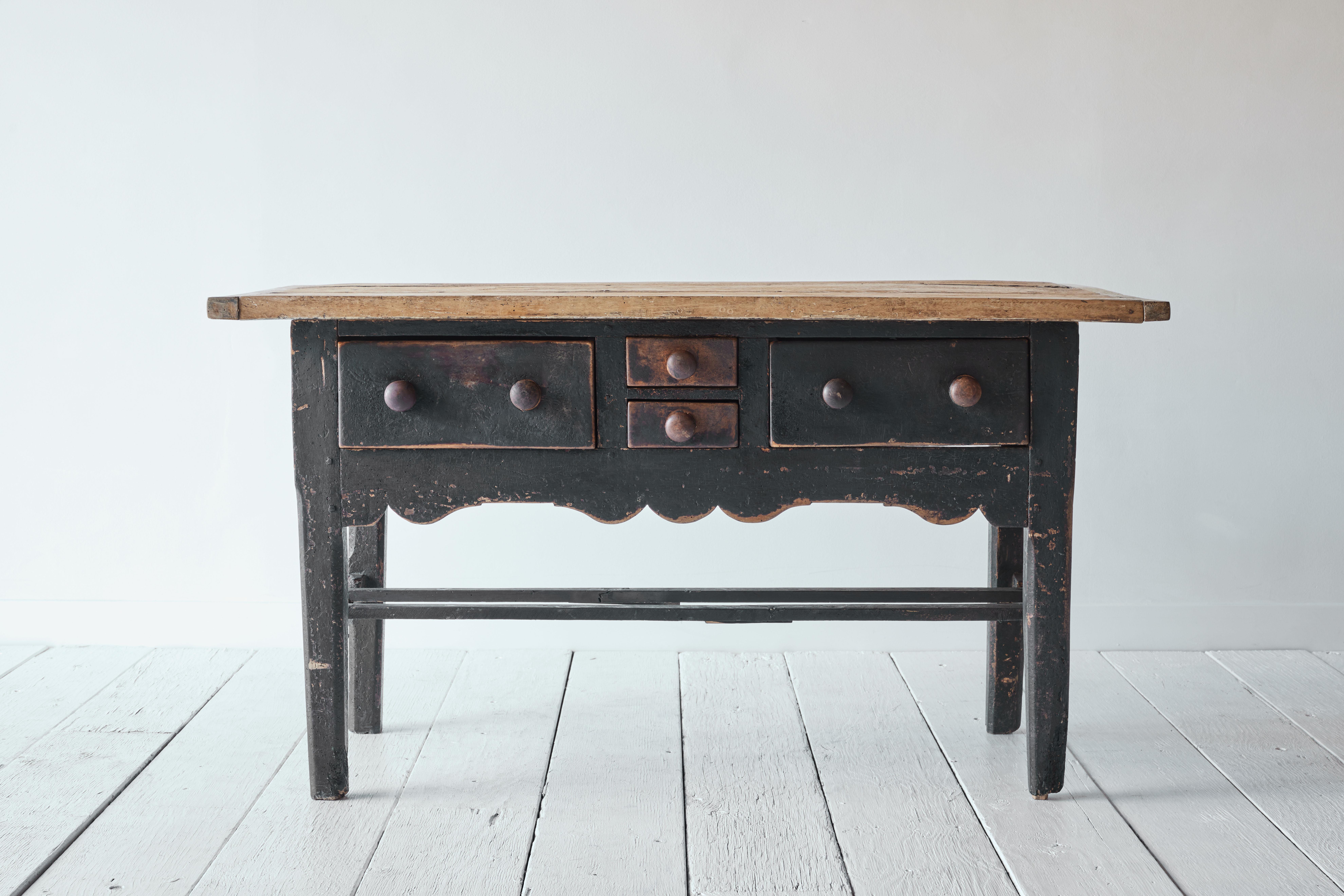 A unique 19th century French work table with black painted base and natural wood top. This table features four drawers, an intricately carved skirt and two bottom trestles. This is the perfect piece for a kitchen island or a side table and has been