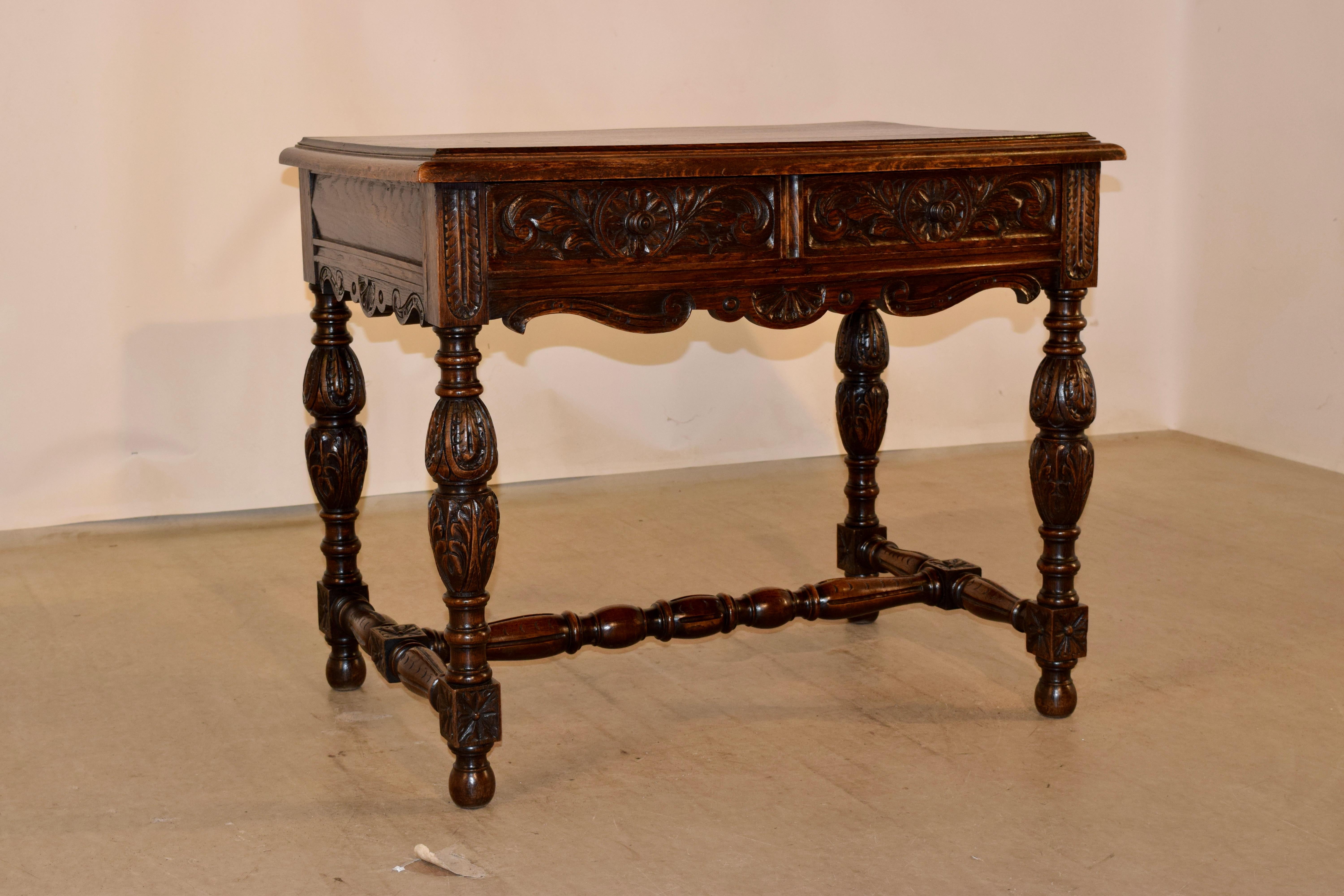 19th century oak writing table from France with a beveled edge around the top, following down to paneled sides and hand carved and scalloped aprons. The front of the table contains two drawers, both with hand carved drawer fronts over and a