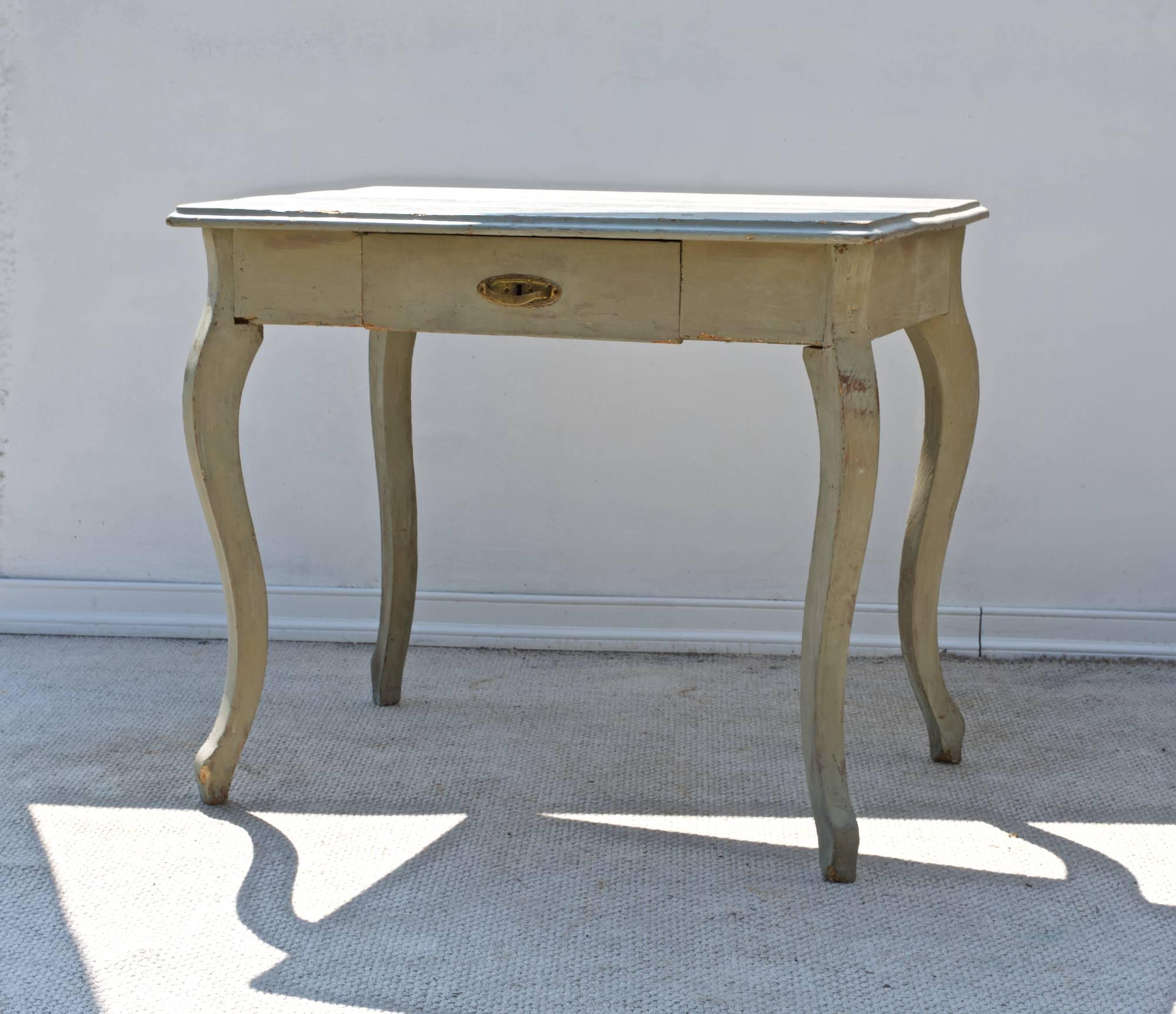 A sweet and curvaceous late 19th century French writing table having an old and fantastic Gustavian inspired paint surface, a three board molded top resting on one short and central drawer that resides above carved and flowing cabriole' legs. The