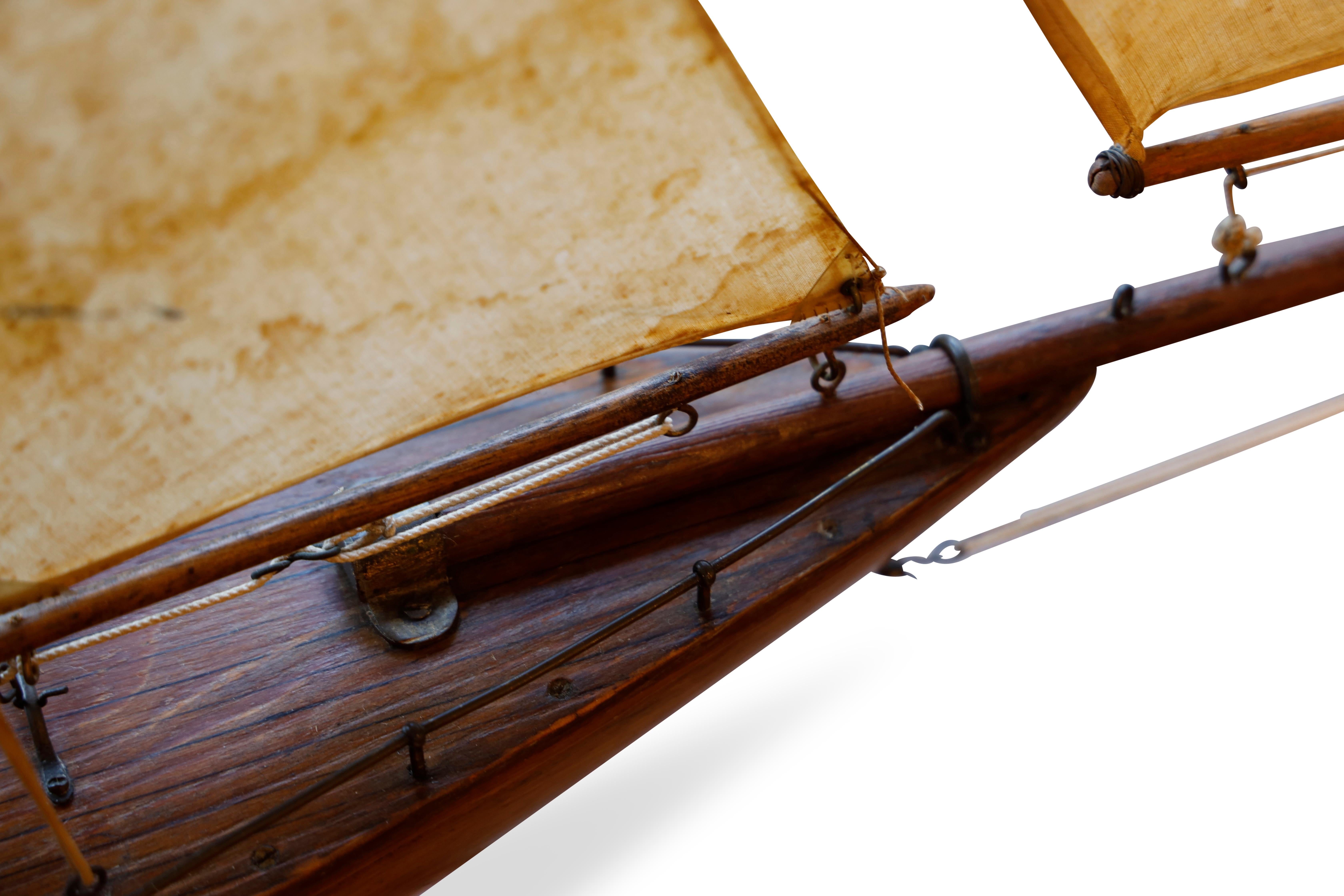Small size gaff-rigged pond yacht.  Made from carved and hollowed wood with copper keel with lead bar weight and rubber support to silvered rudder.  Deck is scored and fitted with brass deck rails, mast sockets and boom rings. Racked mast with yards