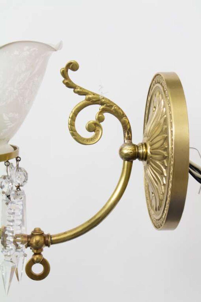 A pair of late 19th century Victorian sconces with curved brass arms, original floral glass, and crystals. These were made in the US. The arms are a smooth brass with a light foliate flourish. The glass is acid etched with a floral design and