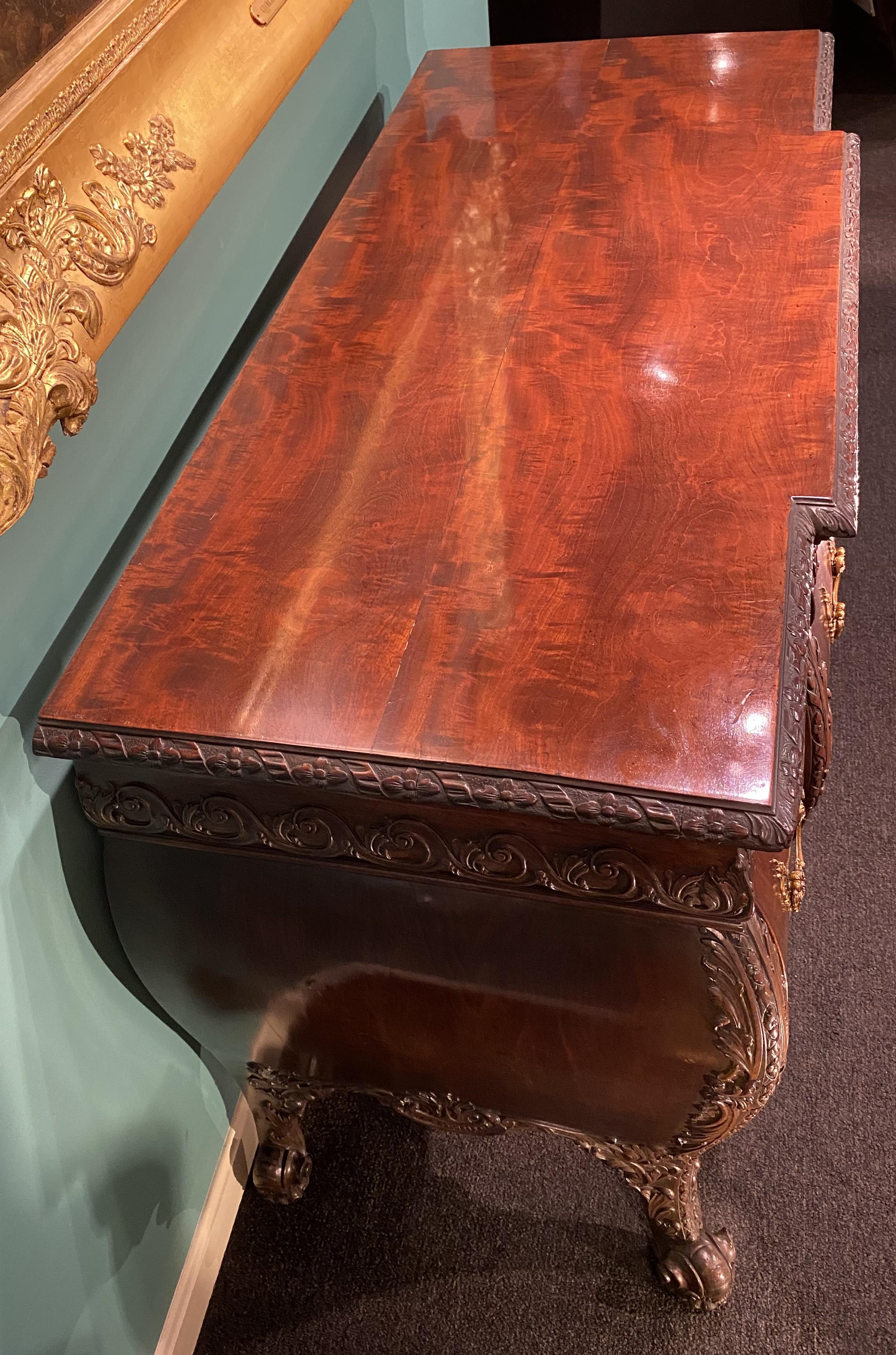 An exceptional example of a George II style carved mahogany commode in the manner of Thomas Chippendale with foliate carved top and conforming bombe style case with scroll carved frieze decoration, three fitted frieze drawers over six fitted deeper