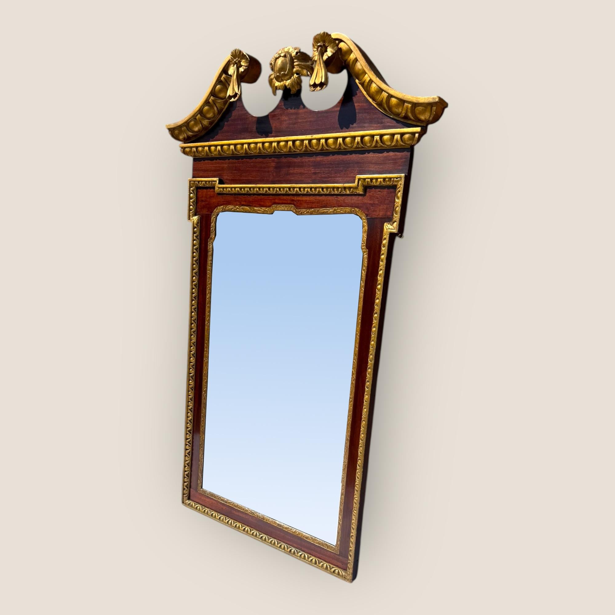 Specchio da parete in stile Giorgio II del XIX secolo, dorato e in mogano. Nella parte superiore, un frontone a collo di cigno intagliato e dorato e uno scudo centrale. I lati sono decorati con modanature intagliate e dorate.