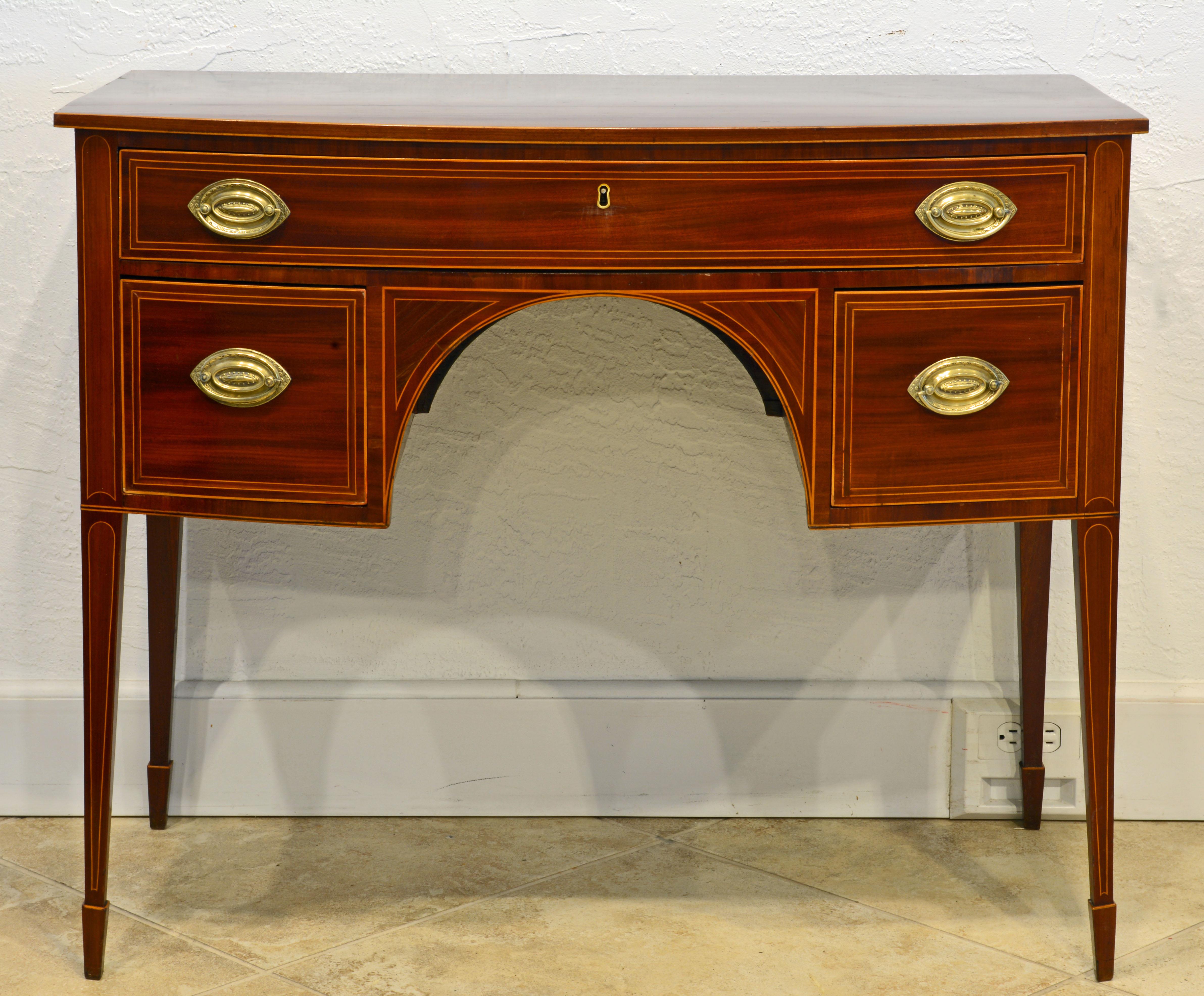 This superior Gerogian bowfront writing desk features a one piece polished satinwood stringed mahogany top above a body with a long drawer and two short deep drawers flanking a semi circular knee hole. The desk rest on four slightly splayed square