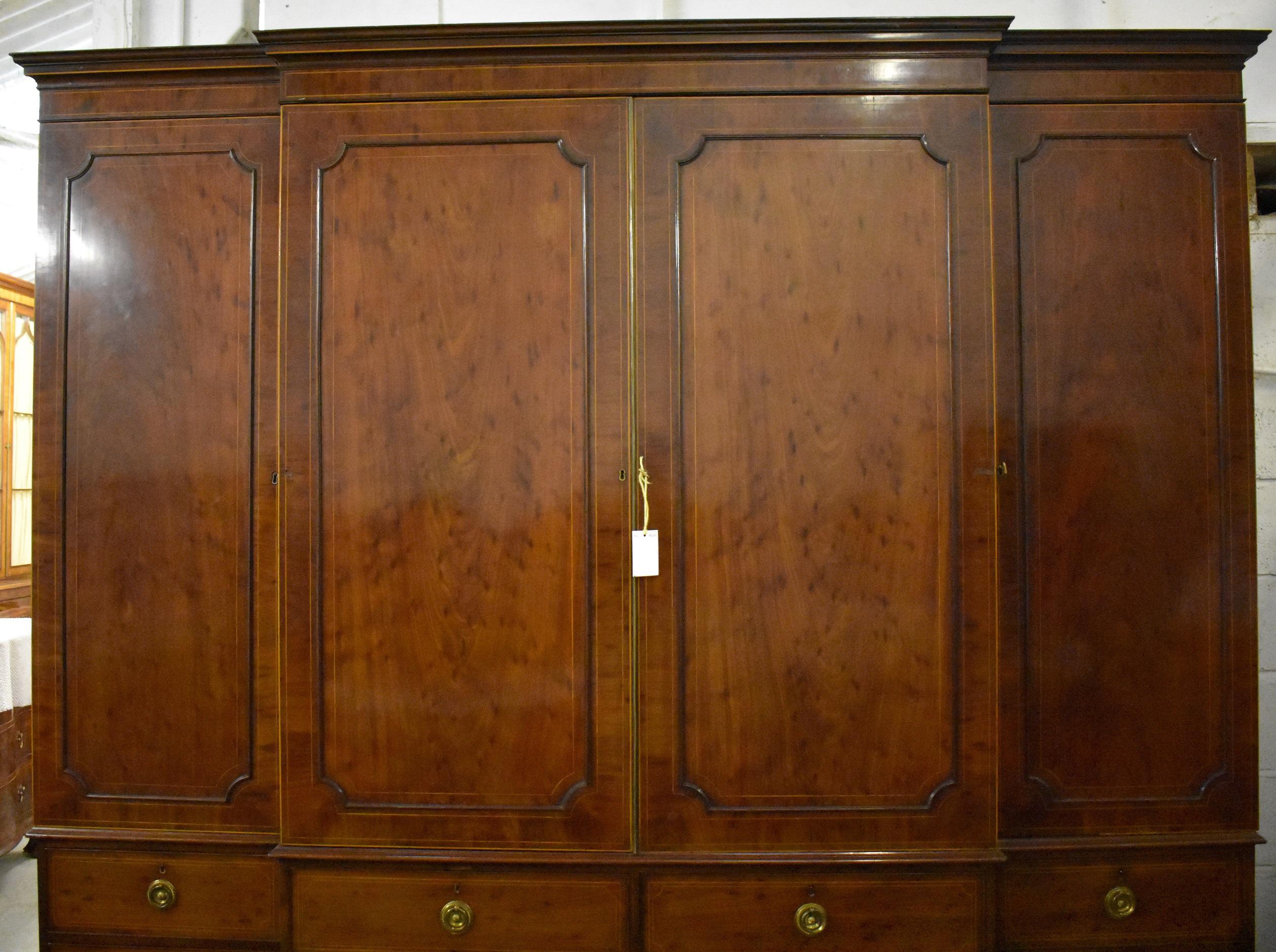 Large George III mahogany breakfront wardrobe. The wardrobe has a flared cornice over four doors, opening to reveal ample hanging space on each end, the centre doors open to reveal multiple adjustable/removable trays. This is above drawers in the