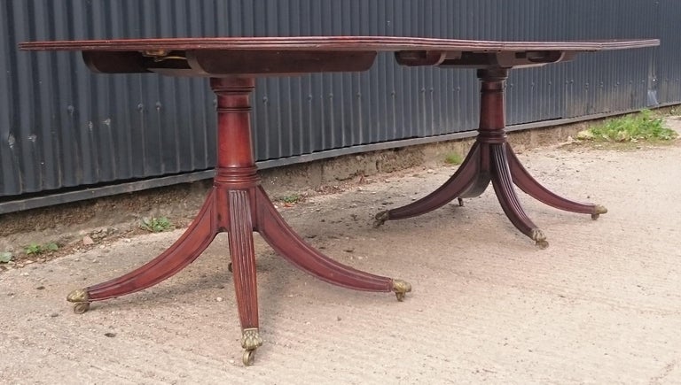 Early 19th century George III period mahogany twin pedestal antique dining table. This table can be made larger with the addition of another leaf. The top can be repolished which will greatly improve the color. At the moment the varnish is hiding
