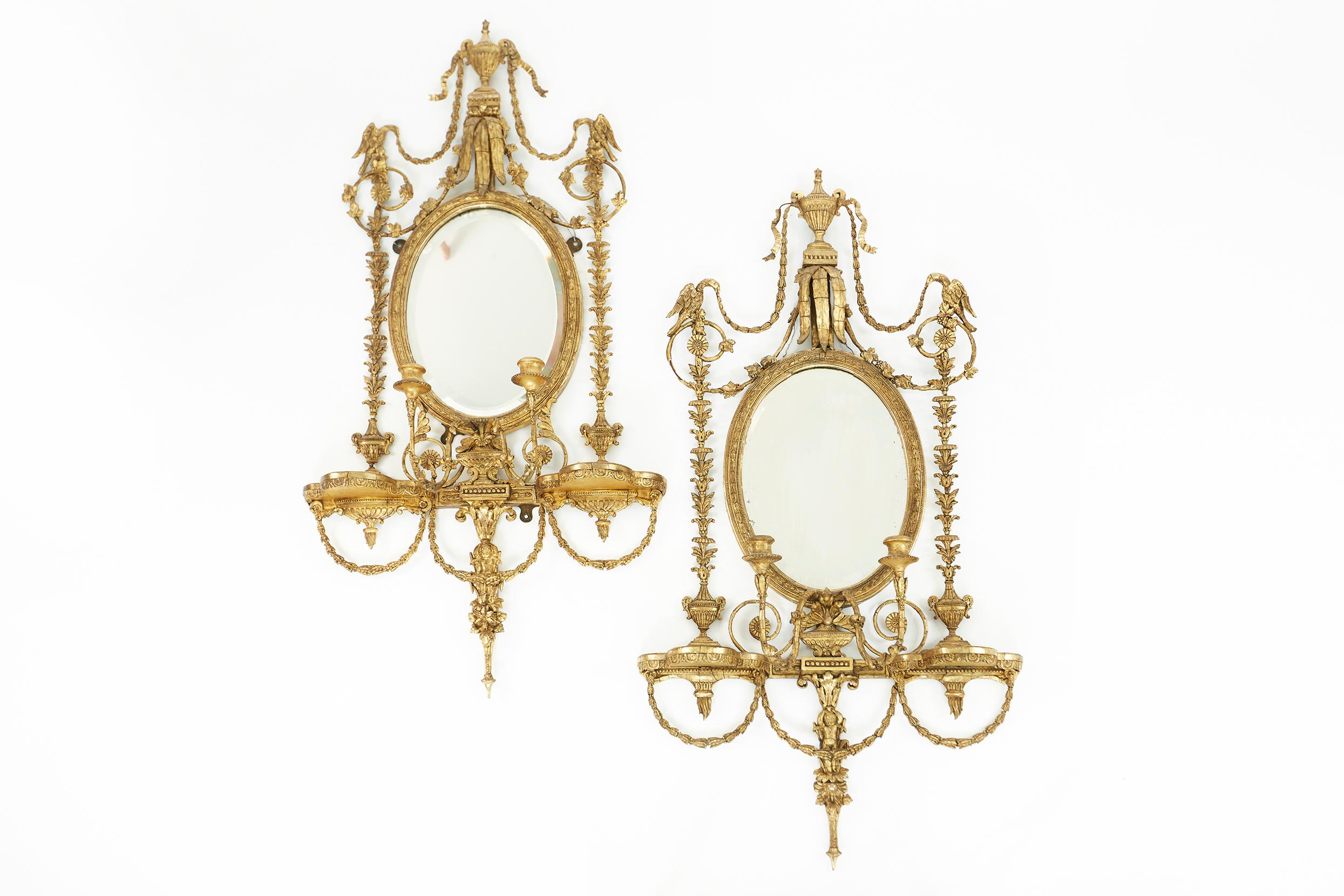 19th century George III style giltwood framed girandole pair mirror . Each one feature an oval mirror plate within a molded frame surmounted by an urn form crest and swags, the apron with candle arms flanked by shelves. Each one is in good antique