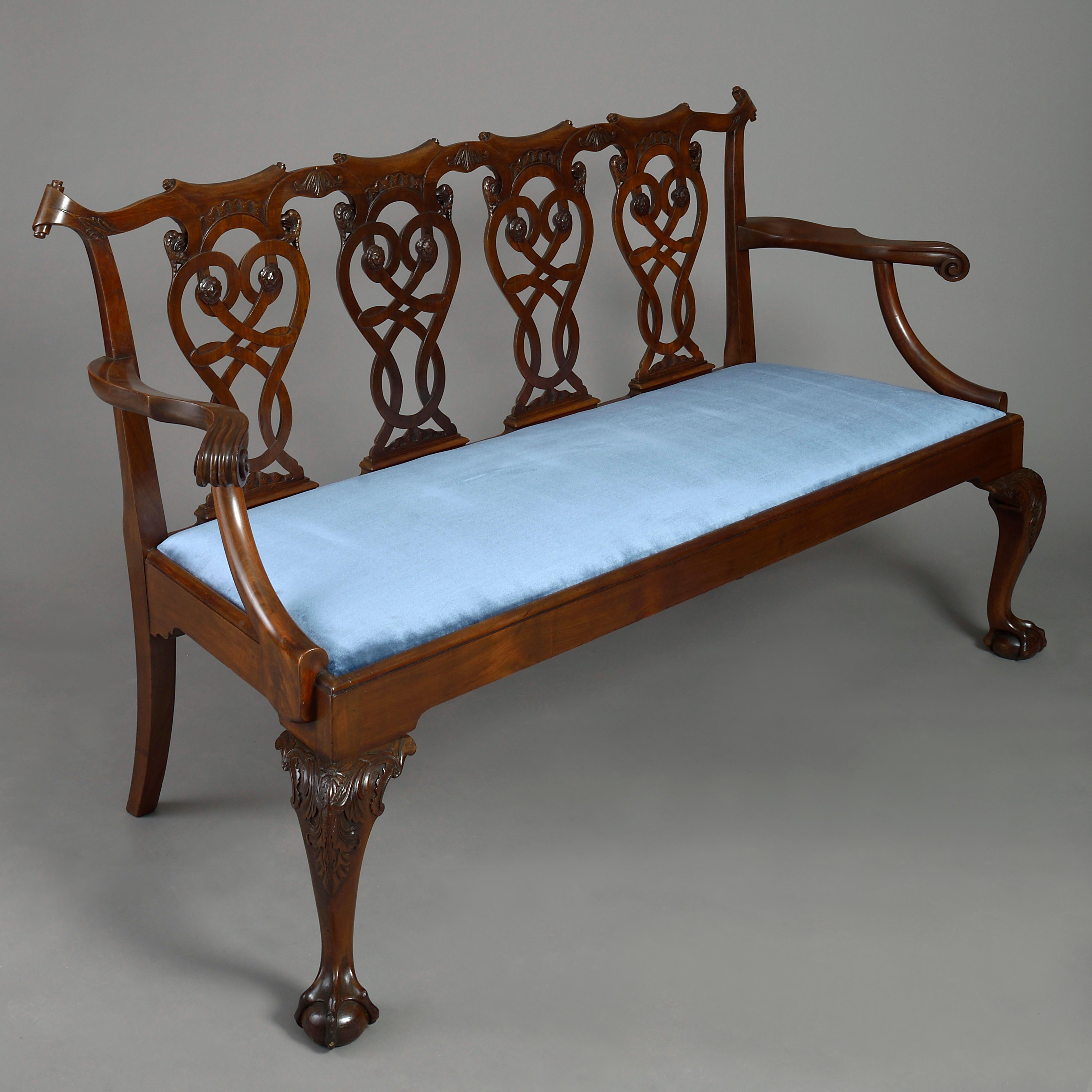 A fine late 19th century mahogany settee in the Irish George III manner, the quadruple pierced splat back with carved scrollwork, eagle heads, rocailles, and rosettes, the scrolling arms set upon a frame with drop-in seat, all raised on acanthus