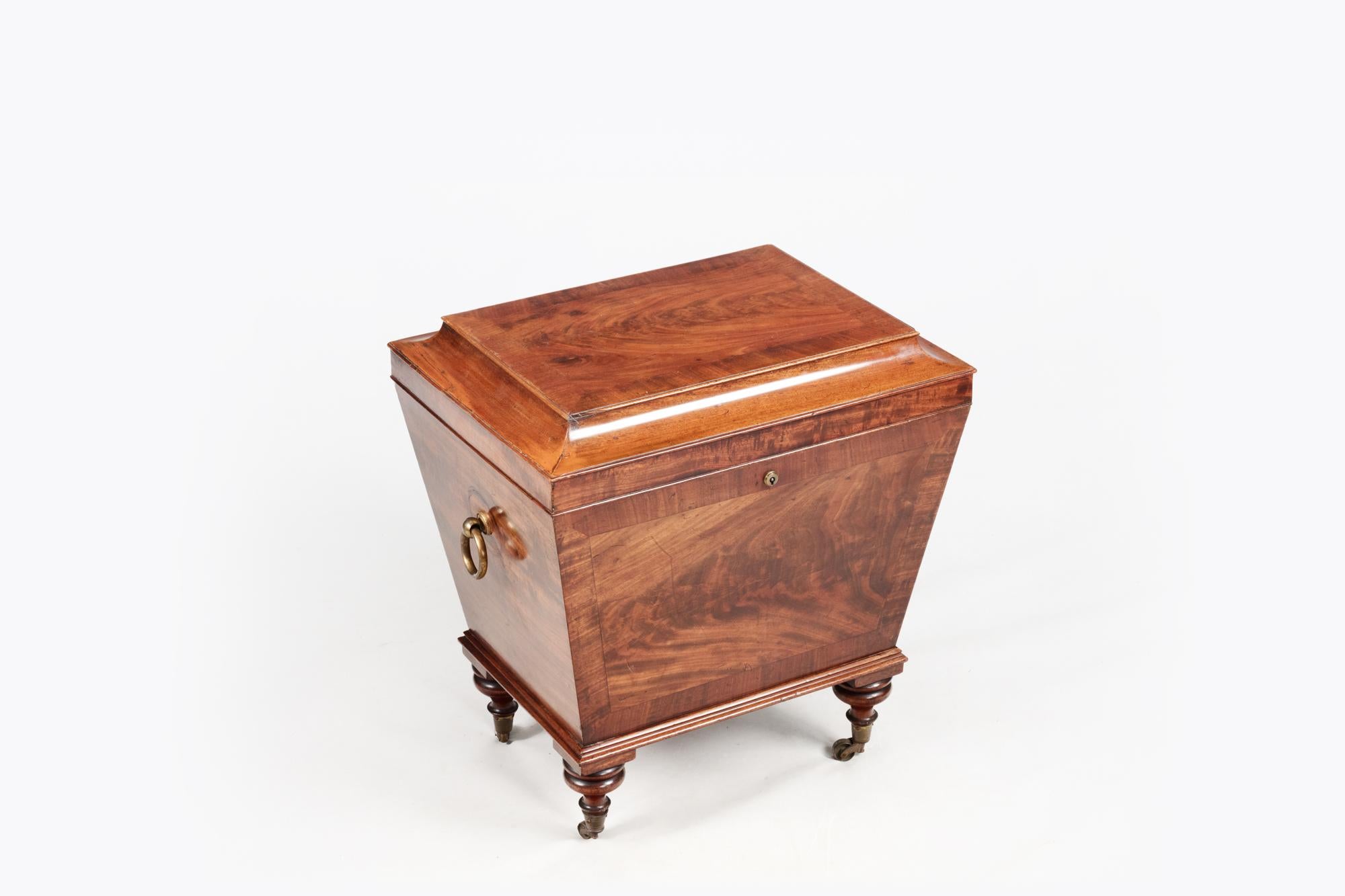 19th Century George IV mahogany cellarette, or vin de garde, of sarcophagus form, with hinged lid and brass side carrying handles, raised on castors. Featuring a flat rectangular top with corners that taper down to the fore-edge of the top. At the