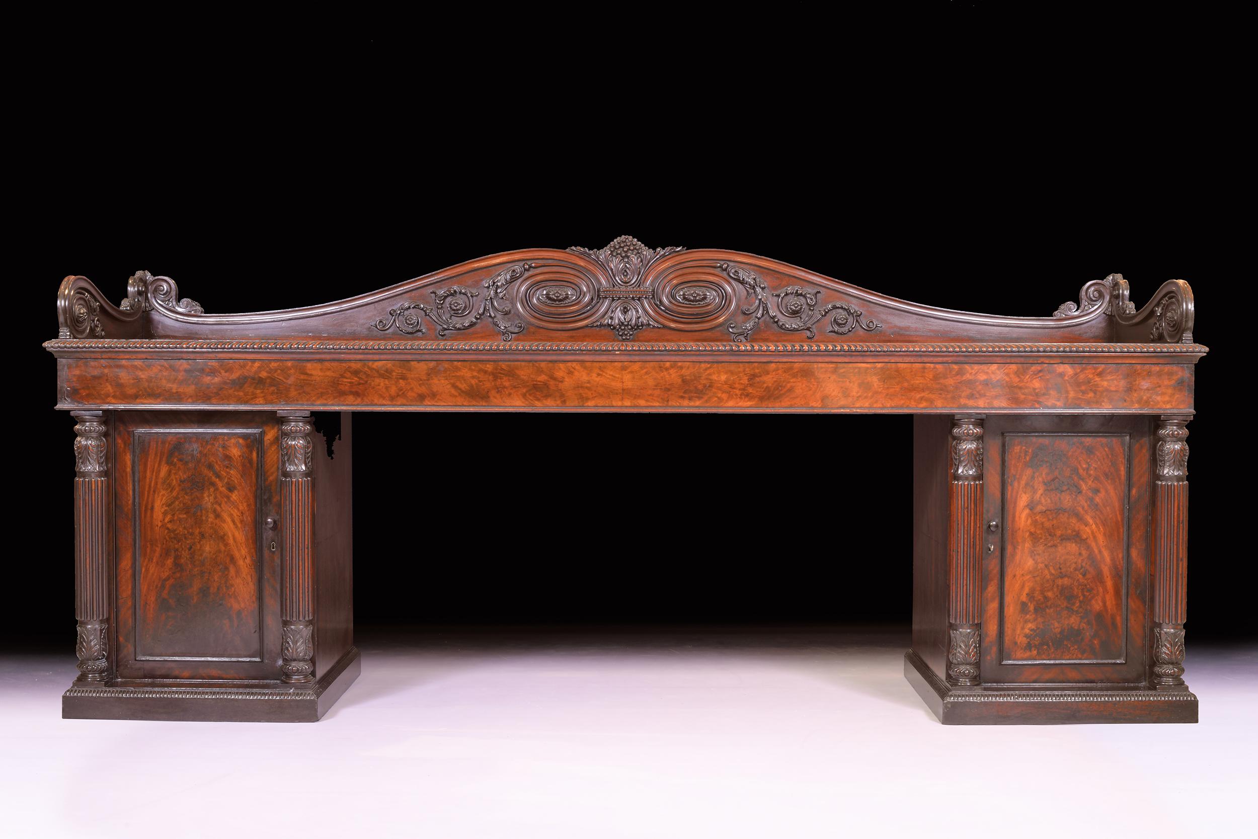 An exceptional quality mahogany monumental George IV figured mahogany pedestal sideboard attributed to Gillows of Lancaster, the rectangular top with a superbly carved back of Grecian scroll and bunches of grapes, above three frieze drawers, resting