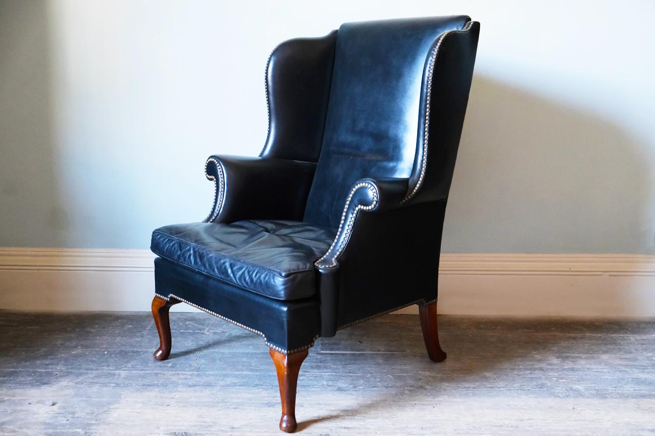 A fully restored Georgian black leather-upholstered wingback armchair outlined with a close nail trim and raised on cabriole legs terminating in scrolled feet.
