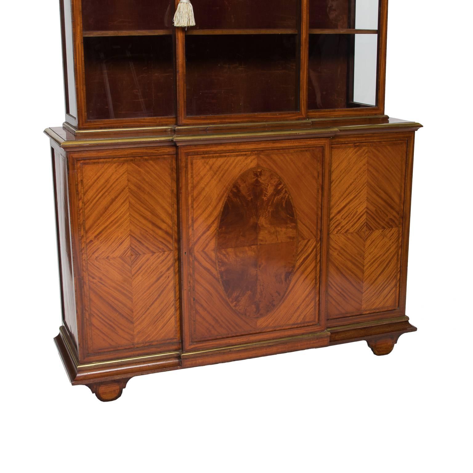 19th century Georgian display cabinet made from highly figured anigre veneer, each panel of the base is bookmatched and the center has a burled oval inlay. The base has one door which opens to storage. The cabinet has a break front to the top and