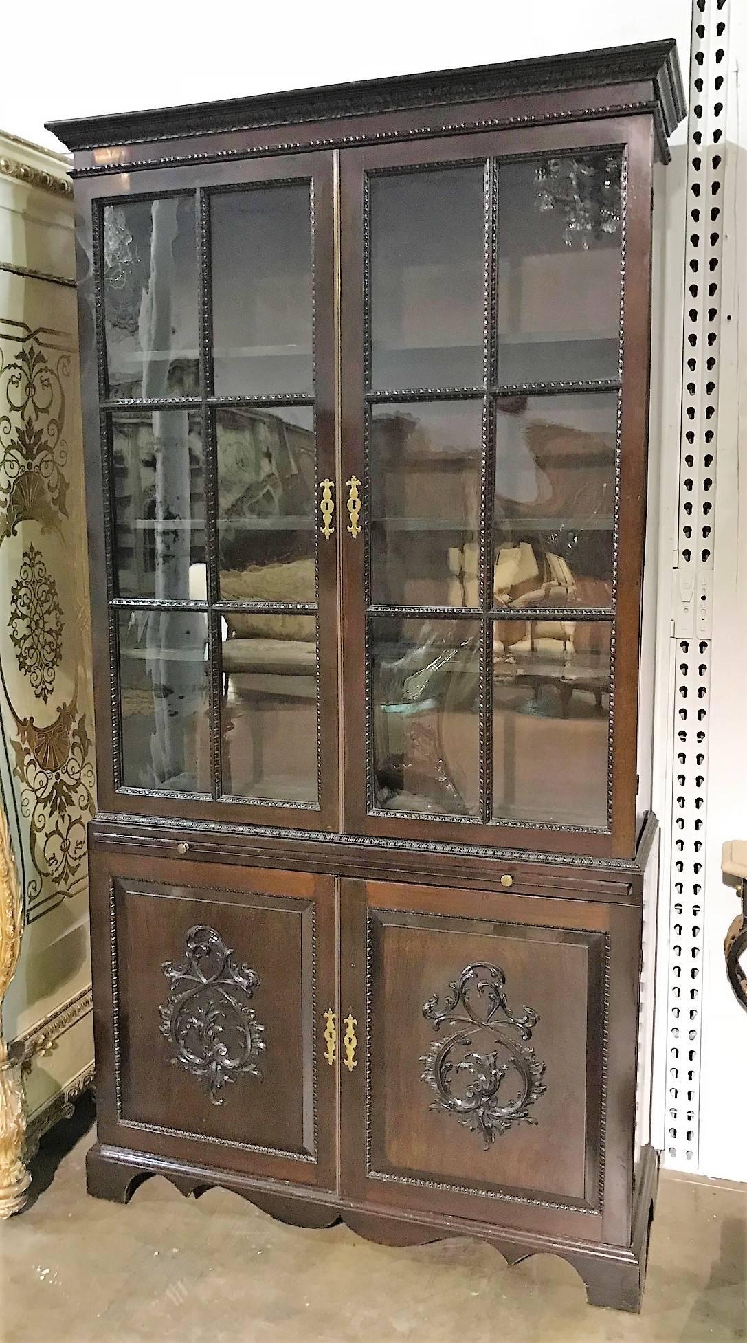 Superb English Chippendale/Georgian design mahogany bookcase with glazed paned double doors with carved moldings atop a pull-out writing slide and raised paneled cupboards having hand-carved leaf scrolls in relief. The entire on shaped bracket