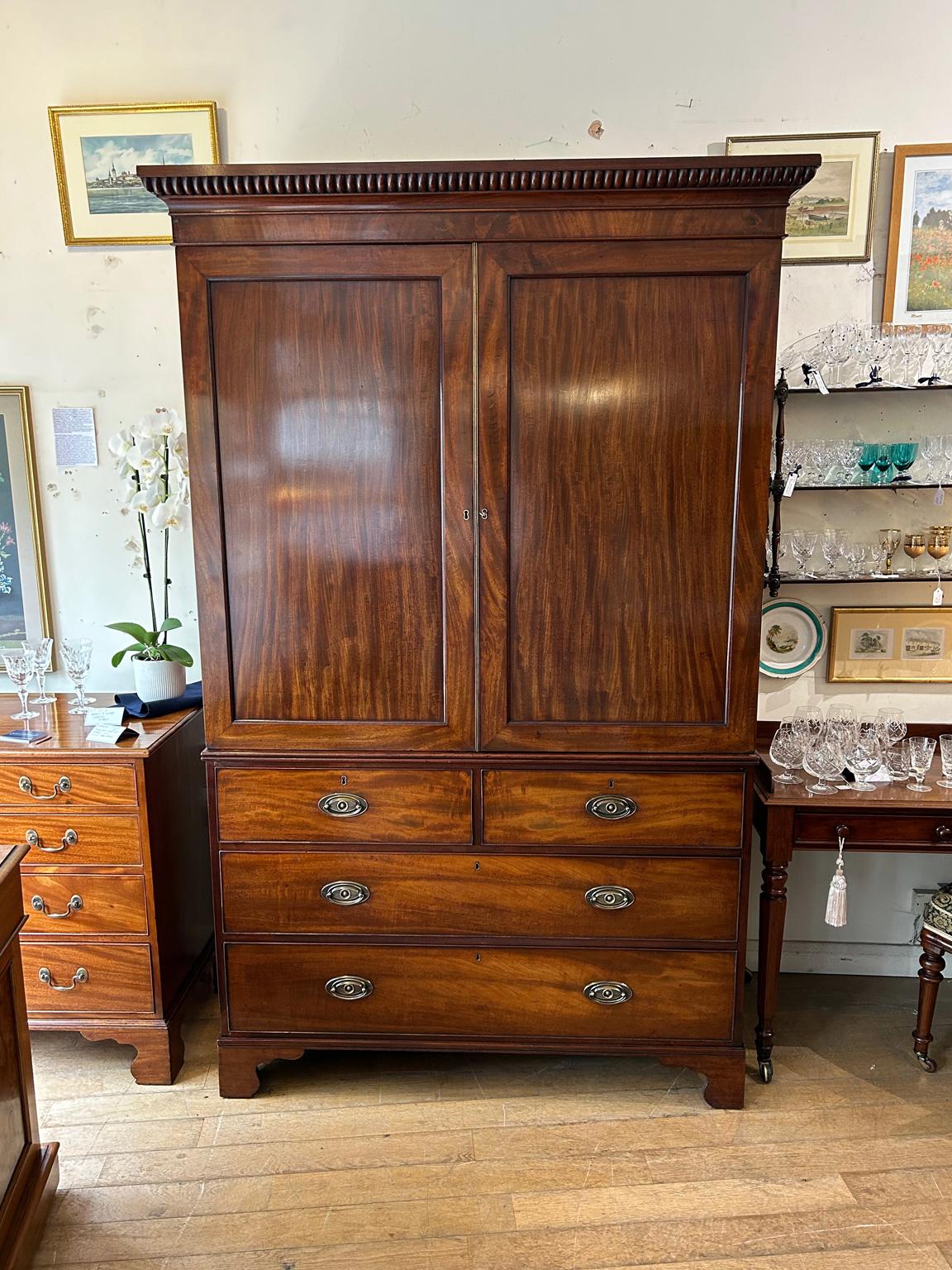 19th Century Georgian Mahogany Linen Press. The inside is fitted with 5 lined cedar wood trays and a brass pole for hanging space. Below has two short and two long solid cedar wood lined drawers with oval brass handles on bracket feet. Comes apart