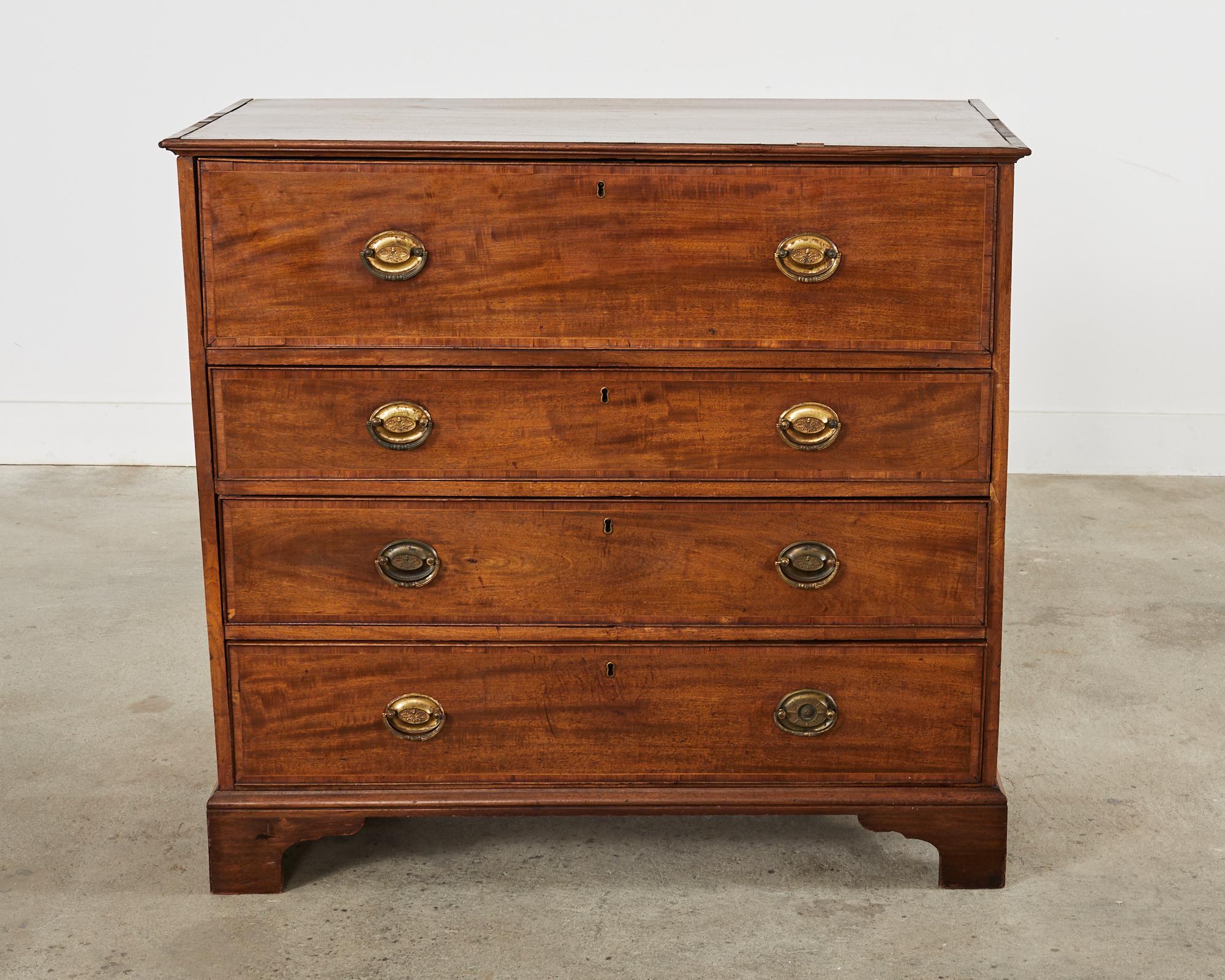 Grand early 19th century English Georgian butler's desk or chest of drawers with secretaire. Crafted from radiant mahogany with delicate thread inlay and veneer. The commode has a large hinged panel with push button mechanisms to drop the front