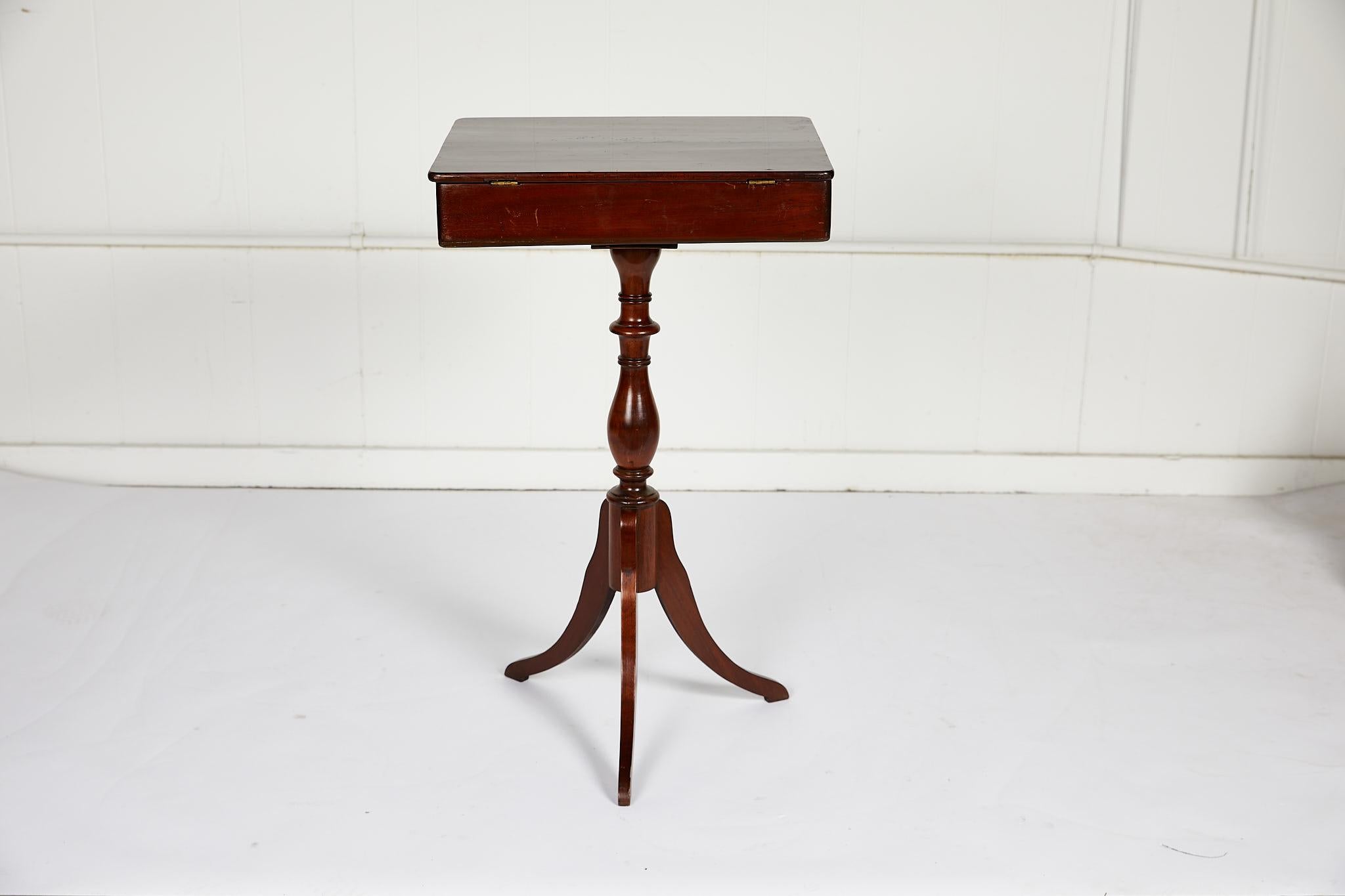 19th century English sewing or side table of mahogany made in the Georgian style. The hinged table top fully opens to reveal a fitted interior within the case. The case rests on a turned baluster column terminating into tripod legs.