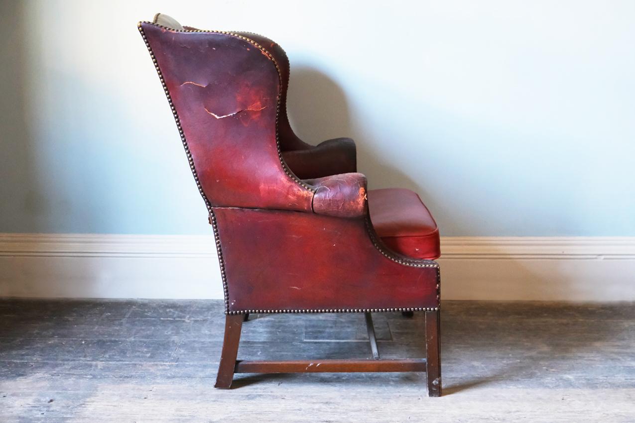 A Georgian red leather-upholstered wingback armchair. 

The chair is outlined with a close nail trim and raised on channeled legs by stretchers.