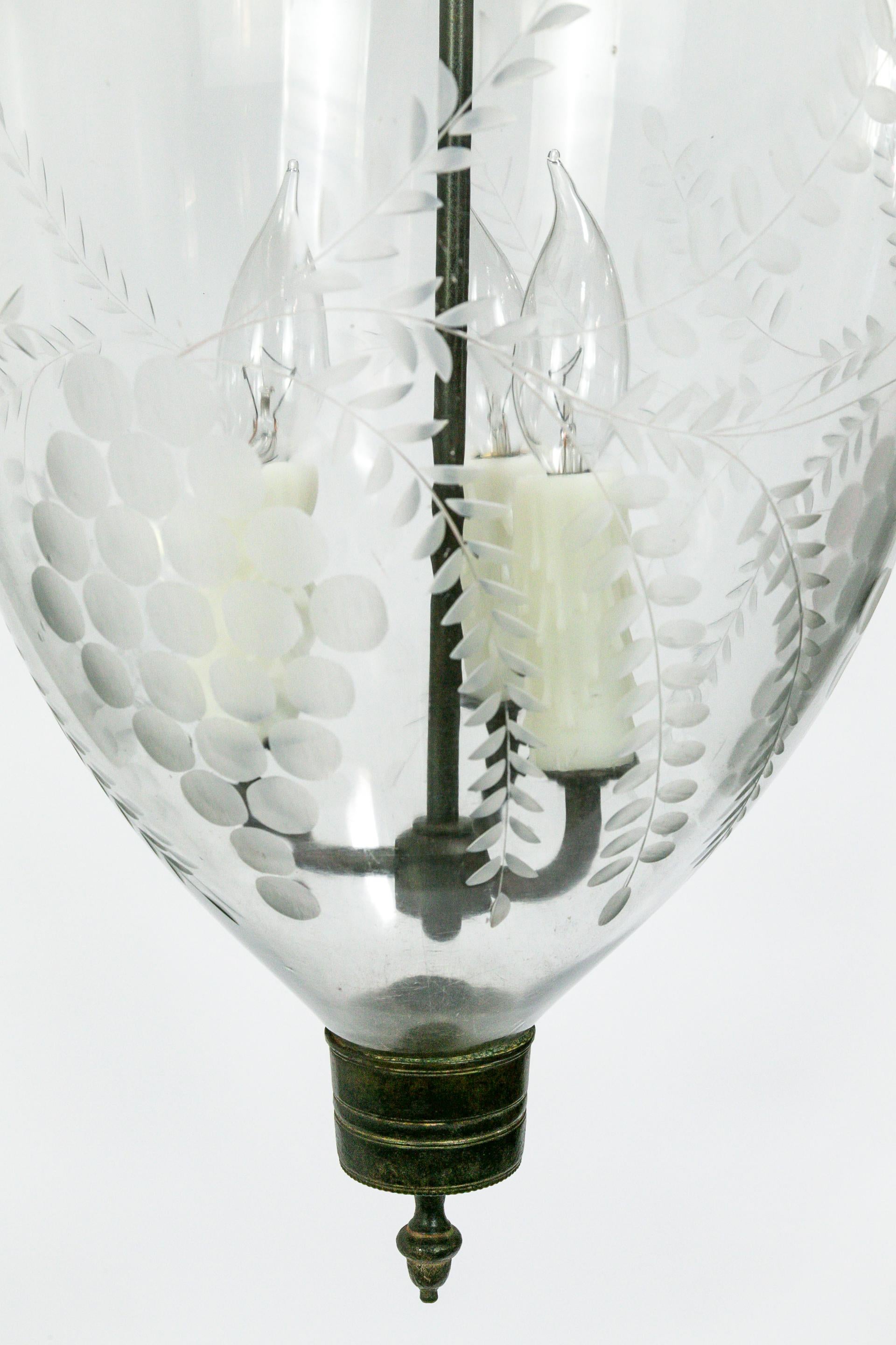 This Georgian style, bell jar pendant lantern is hand blown and etched with a lovely, grape and leaf pattern. The etched smoke bell is particularly notable, with an intricate, flower design. The brass glass holder features bird chain hooks. The