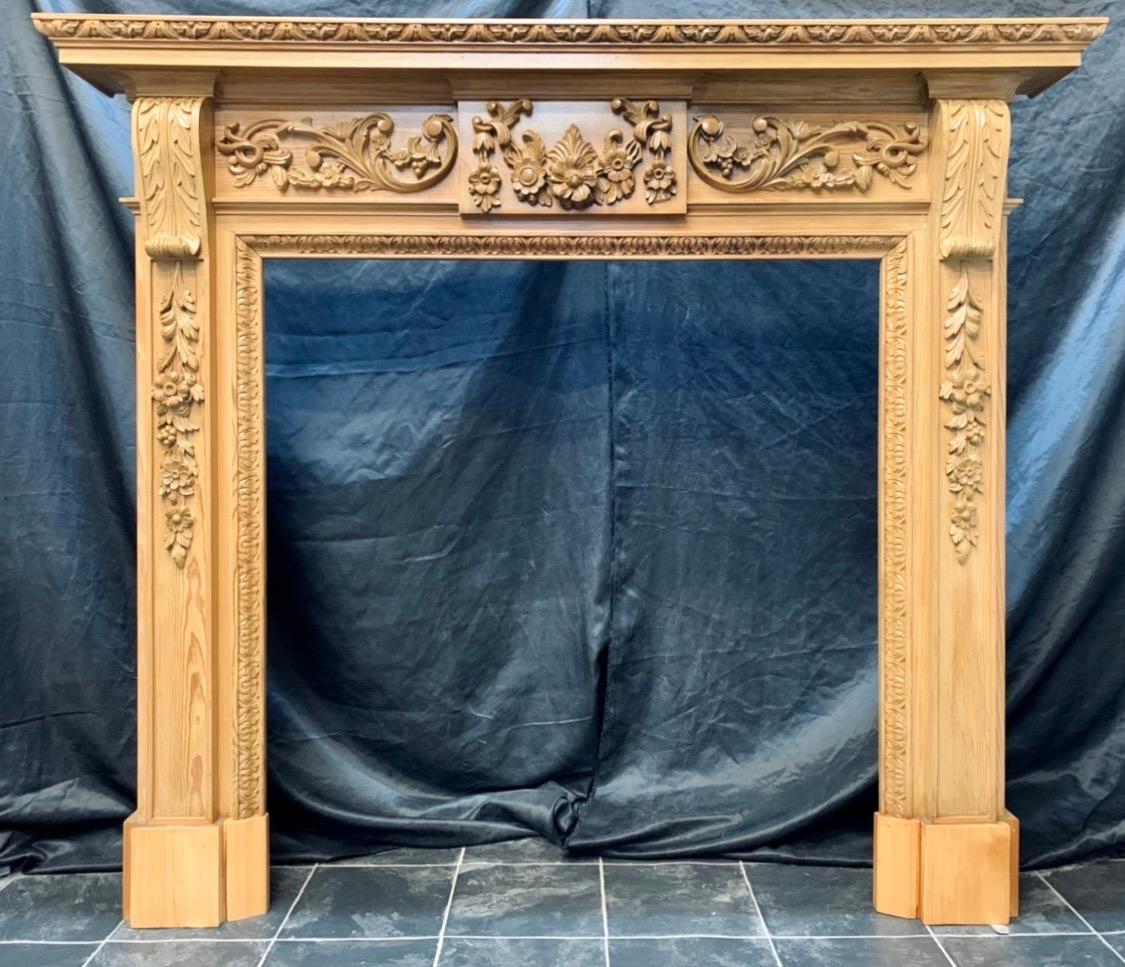 A 19th century Georgian Style profusely carved fireplace surround in a clear wide leaf pine. A generous top shelf with a carved edge detail, a secondary under shelf directly below, all supported by a projecting central tablet with a well carved high