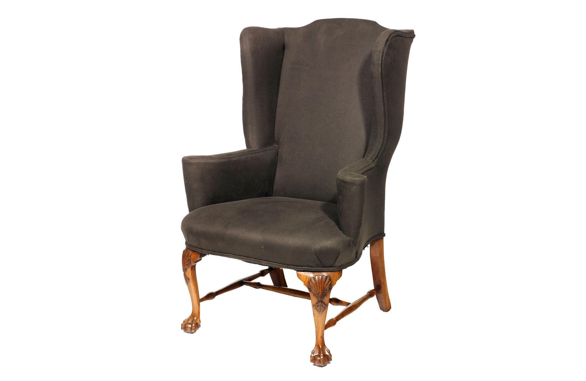 19th Century Georgian wing chair with shaped back and scrolling arms.  Raised on shell carved leg supported by turned stretcher terminating on claw and foot.