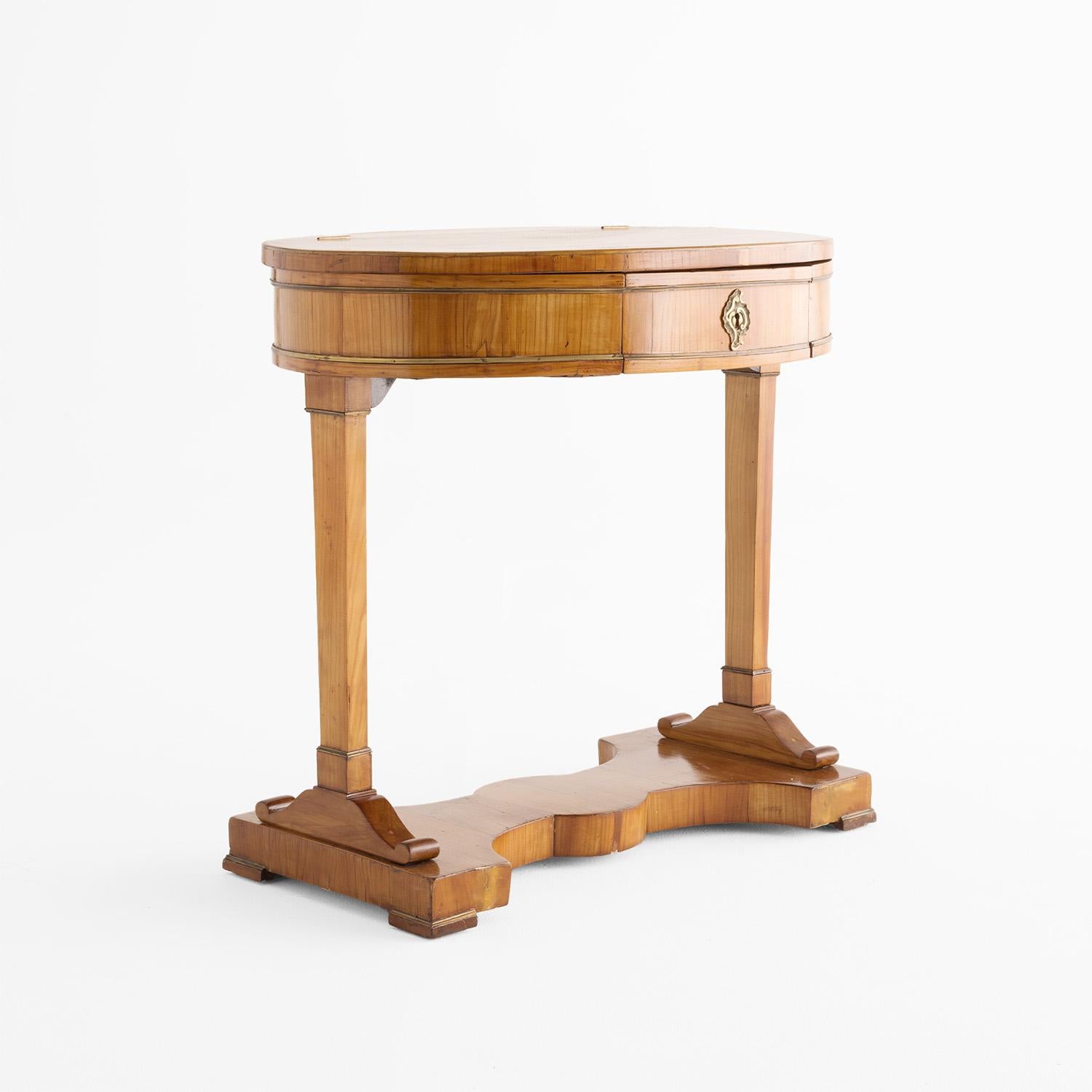 Un antico tavolo da cucito Biedermeier demi-lune tedesco dei primi del XIX secolo, realizzato in legno di ciliegio lucidato a gommalacca e parzialmente impiallacciato, in buone condizioni. La piccola toletta angolare ha un piano semicircolare