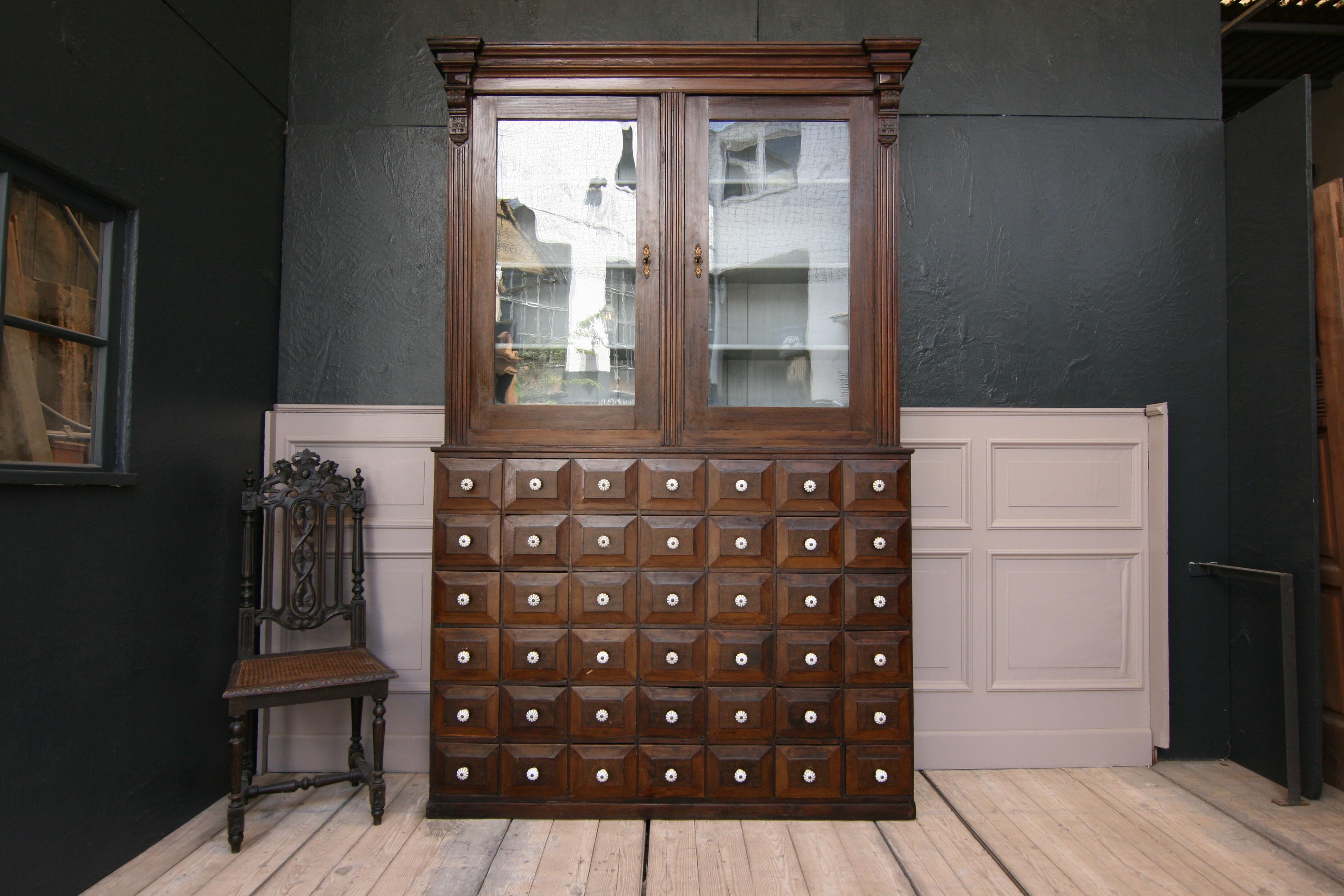 A 19th century German apothecary cabinet made of solid pine wood in the original paint.

2-part body consisting of a lower part (chest of drawers) with 42 drawers with porcelain buttons and a display case with 2 separately lockable doors with the