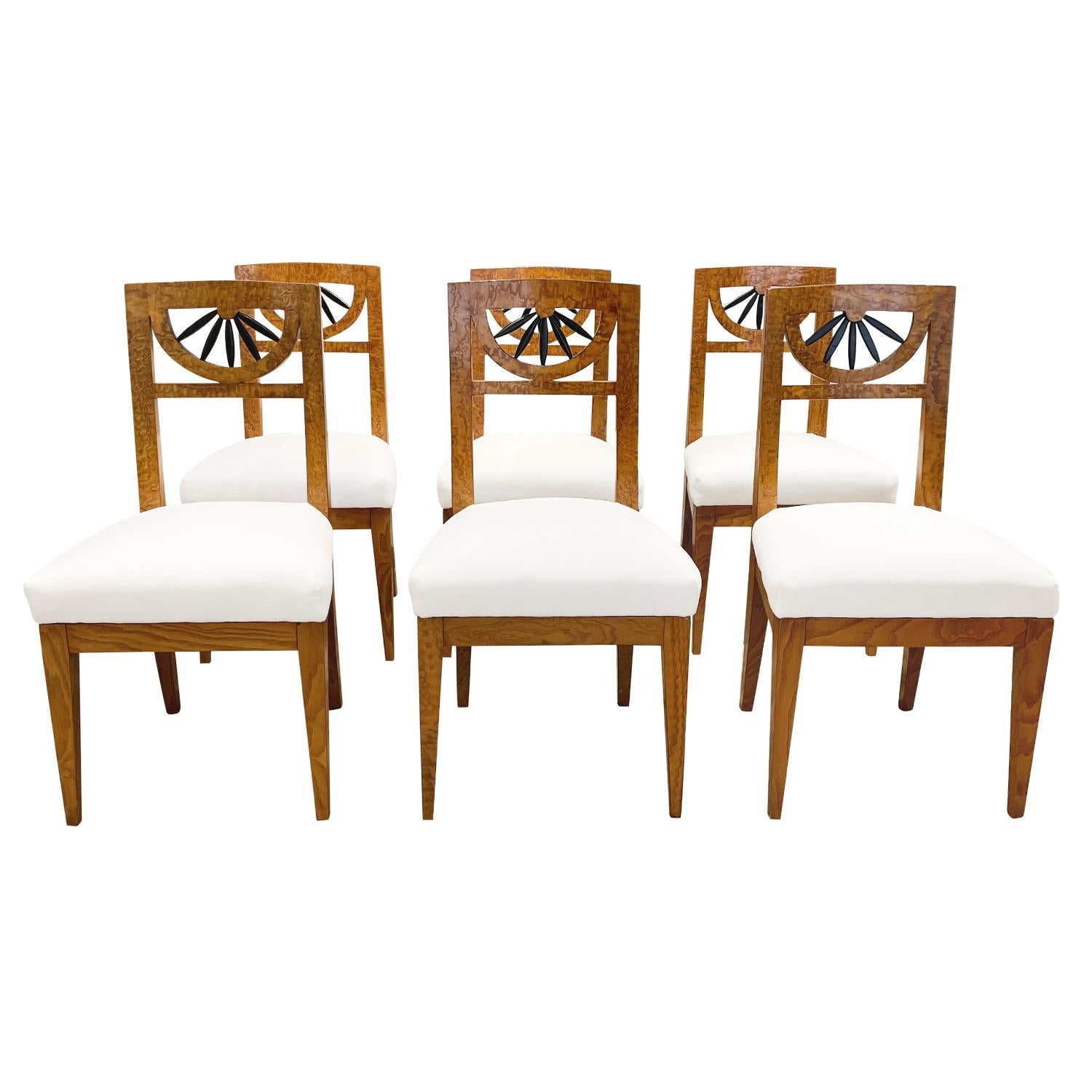 A light-brown, antique German Biedermeier set of six dining room chairs made of handcrafted polished, partly veneered Birchwood, in good condition. The detailed side chairs have an open, arched backrest enhanced by detailed flower carvings which is