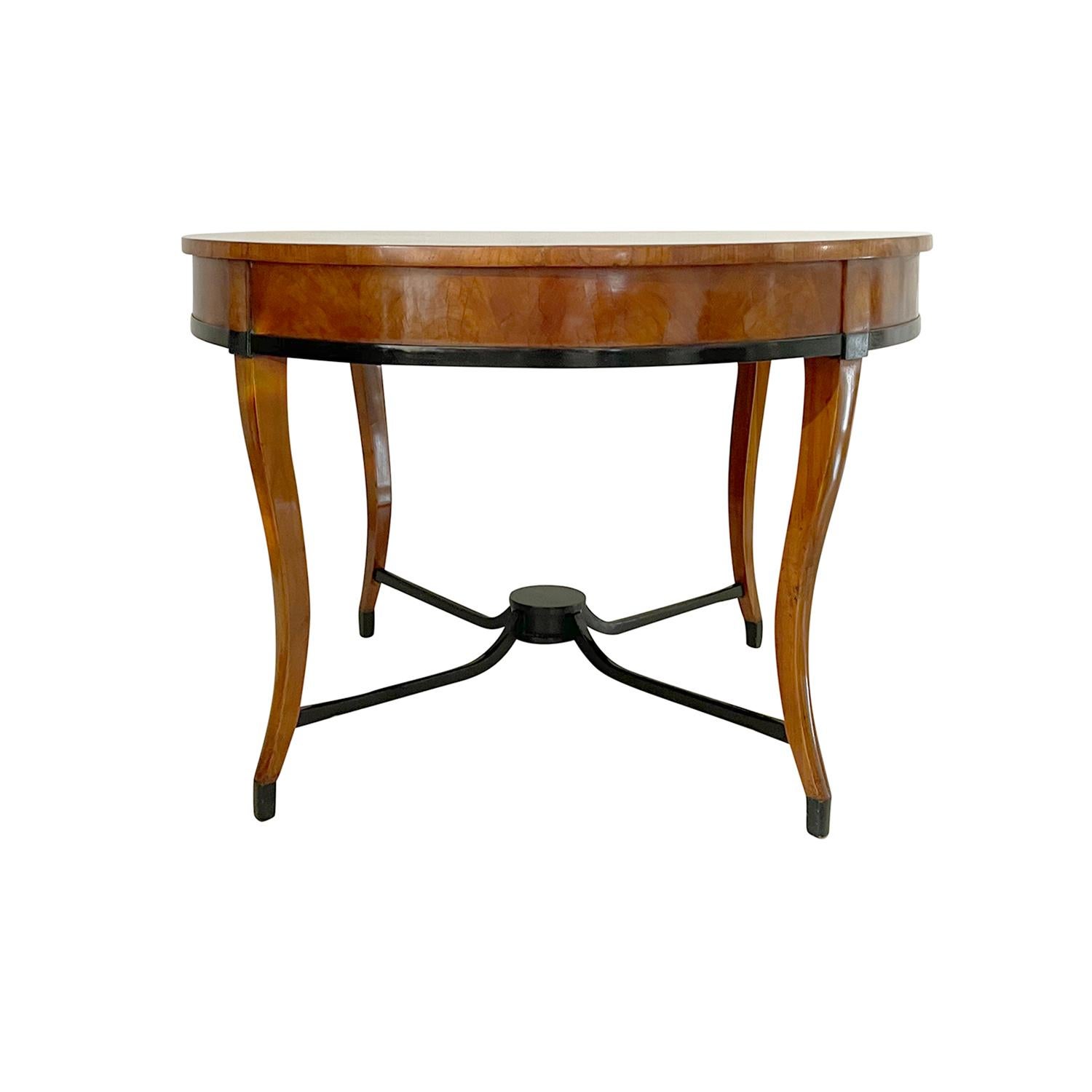 A light-brown, antique German Biedermeier dining room table made of hand crafted Cherrywood, shellac polished and partly veneered in good condition. The round center table is supported by four black ebonized cross beams, standing on four slim arched