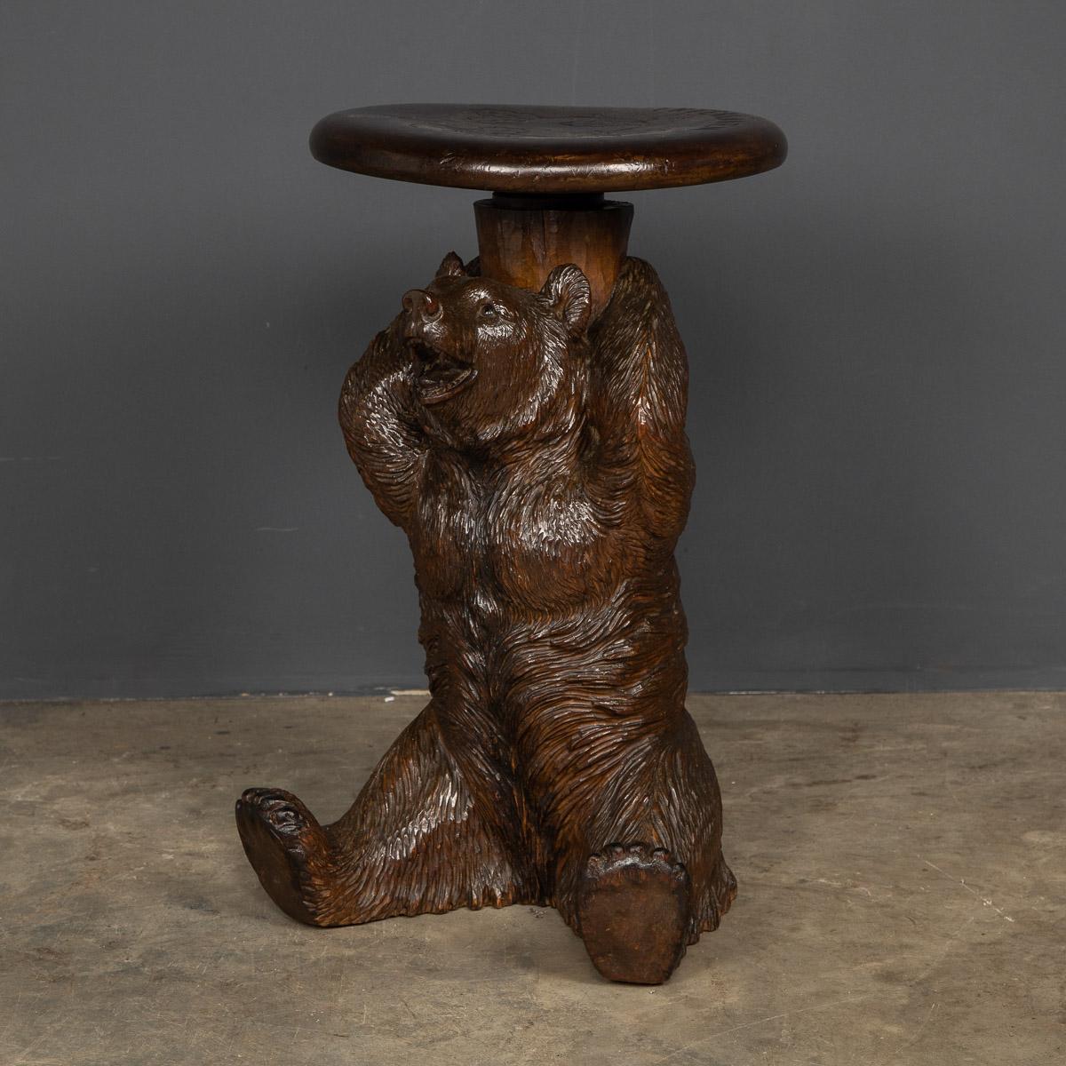 Antique 19th Century German Black Forest carved seated bear holding up a stool, set with glass eyes. Such items were usually bought back by tourists from the Swiss / German borders (the Black Forest) and were a fashionable home decoration accessory