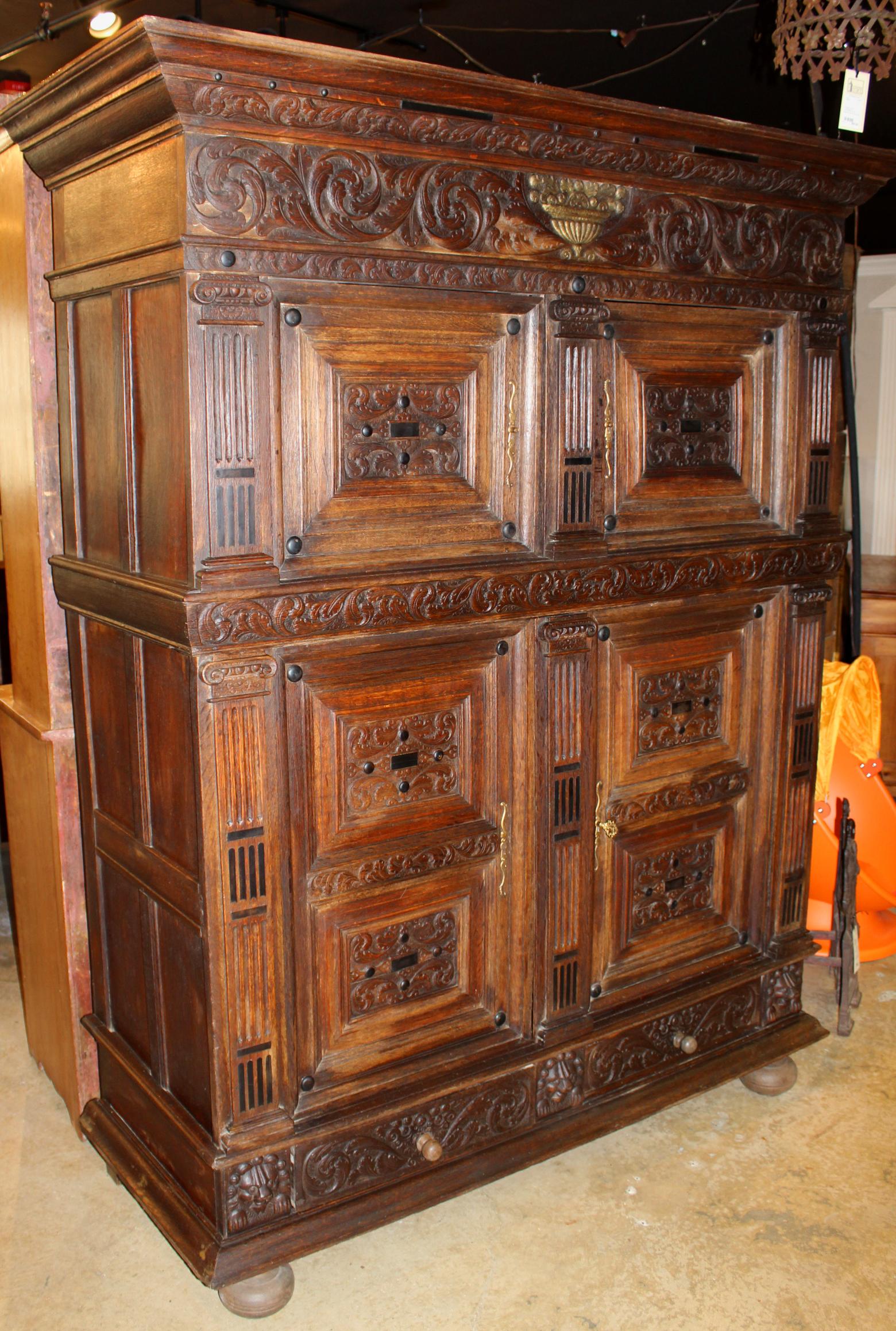 A fine 19th century German two-part oak court cupboard carved in the 17th century manner, the upper case with a molded cornice surmounting a foliate carved case frieze with central gilt compote decoration over two carved panel doors, which open to