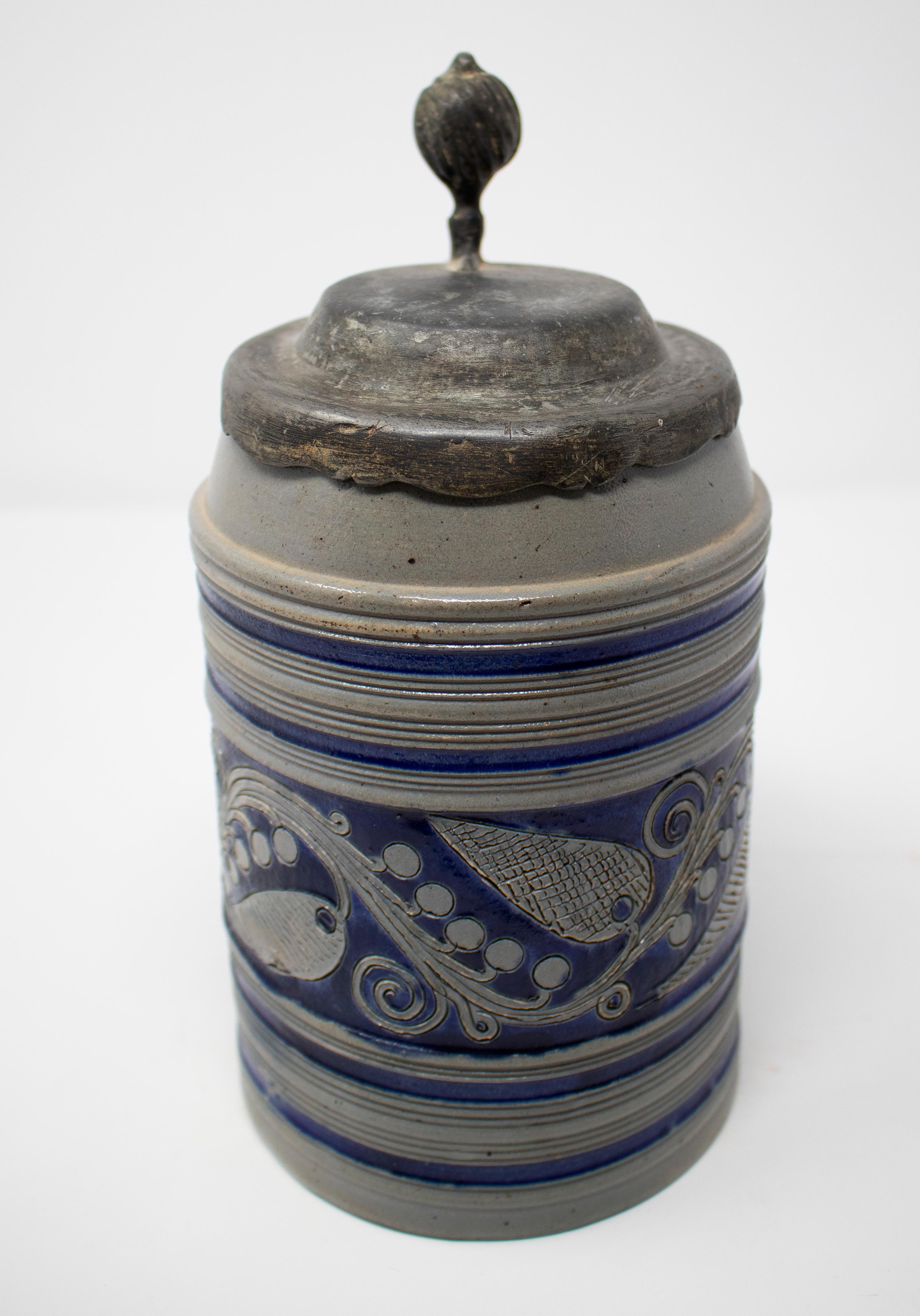 19th century German earthenware beer stein mug with tin lid and cobalt blue ornamental decorations.