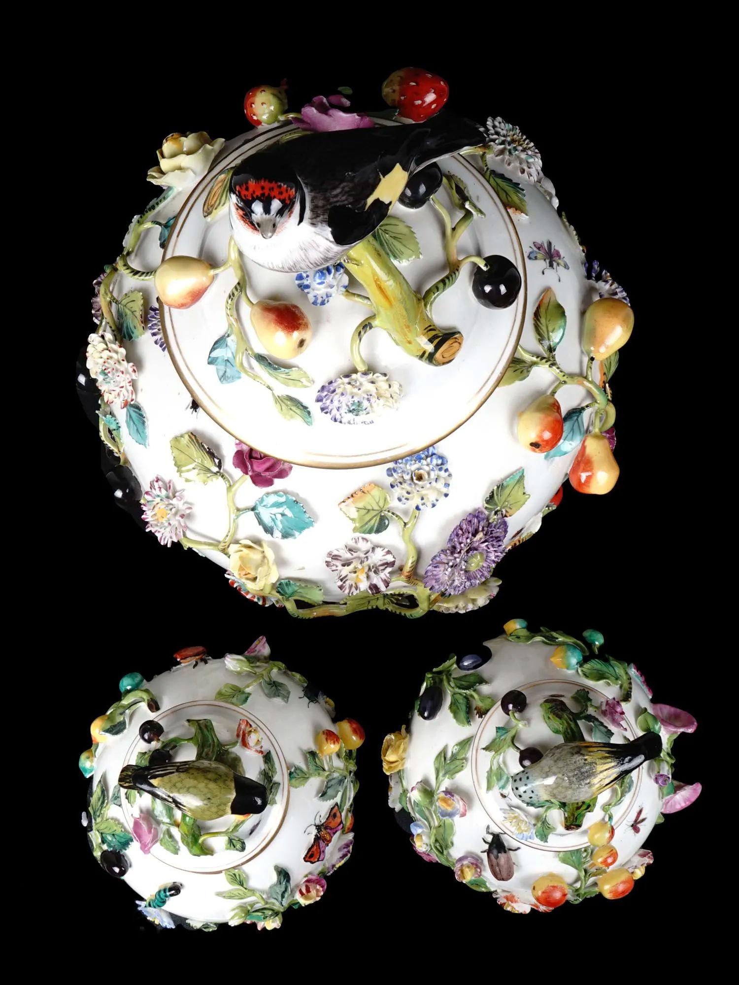 Our garniture from Carl Thieme of Potschappel, Thuringia, near Desdren, includes a large vase with cover measuring 17 inches tall and two vases with covers measuring approximately 11 1/2 inches. Each encrusted with fruit vines and flower heads and