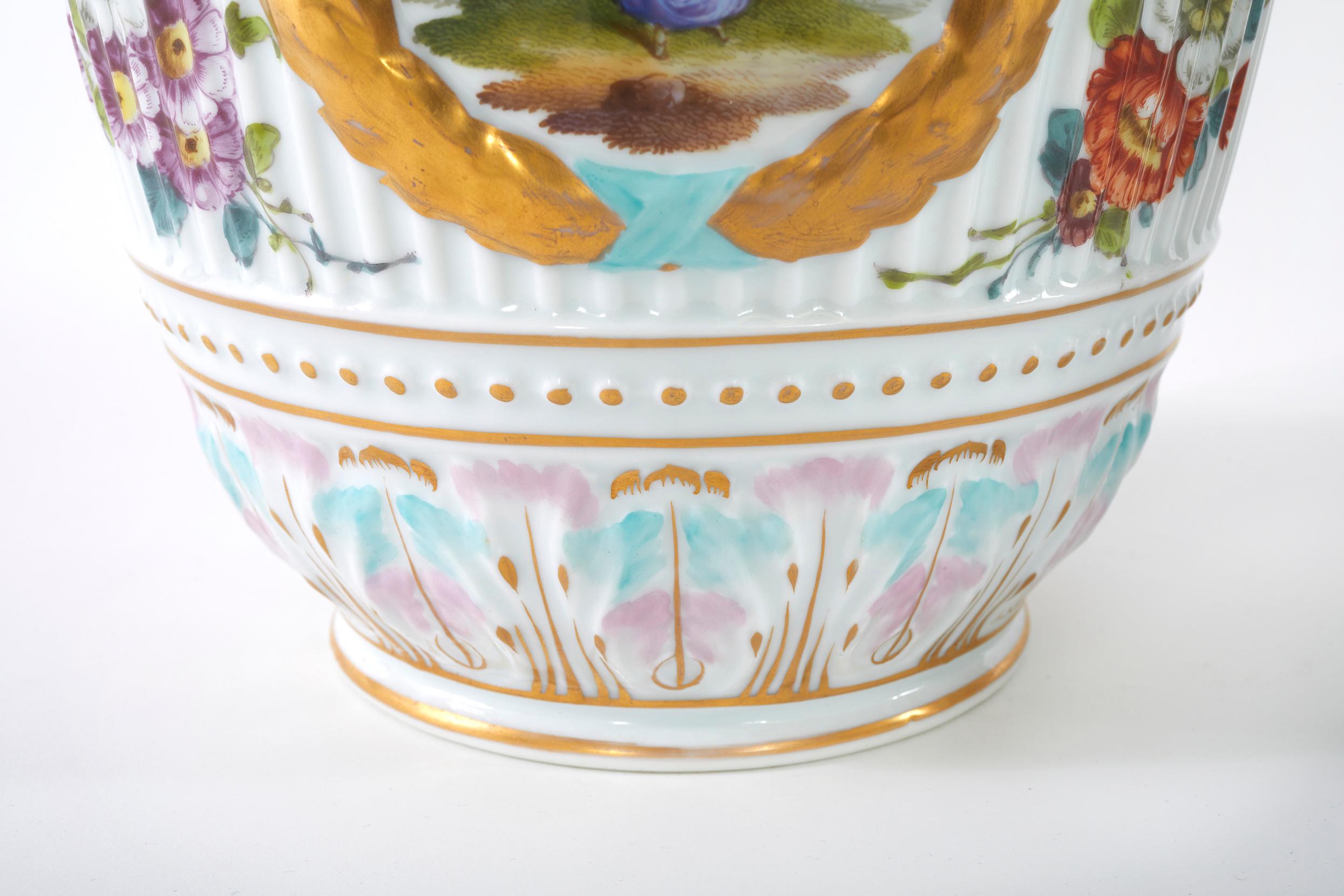 Paire d'urnes / vases décoratifs allemands du 19ème siècle en porcelaine émaillée recouverte de glaçure. Chaque urne présente des détails extérieurs peints de scènes et un sommet recouvert d'un fleuron en forme d'oiseau. Chacune d'entre elles est en