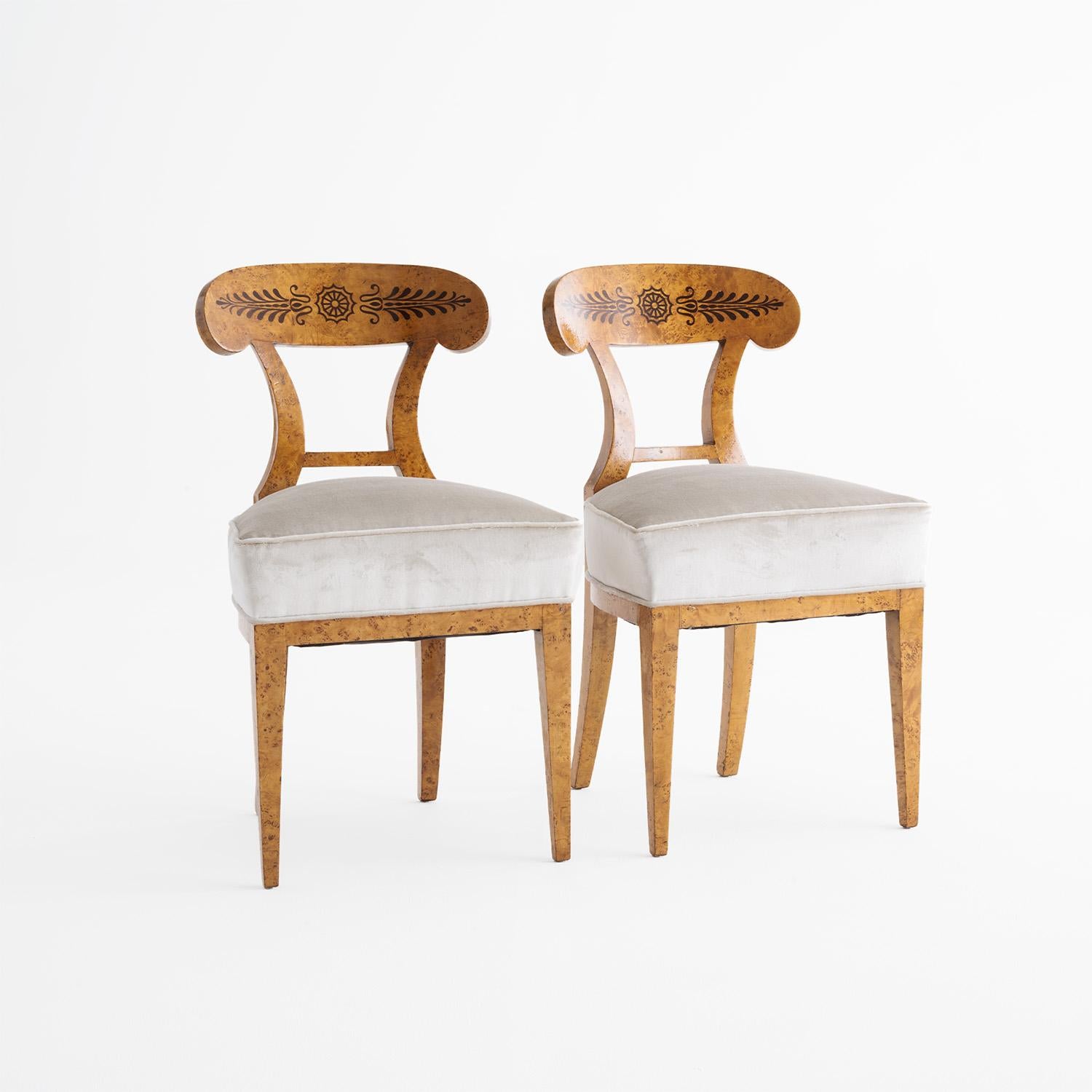 An early 19th Century, antique pair of German Biedermeier dining room chairs made of hand crafted shellac, partly veneered Cherrywood in good condition. The detailed Shovel chairs have an open, arched backrest, standing on four long wooden legs. The