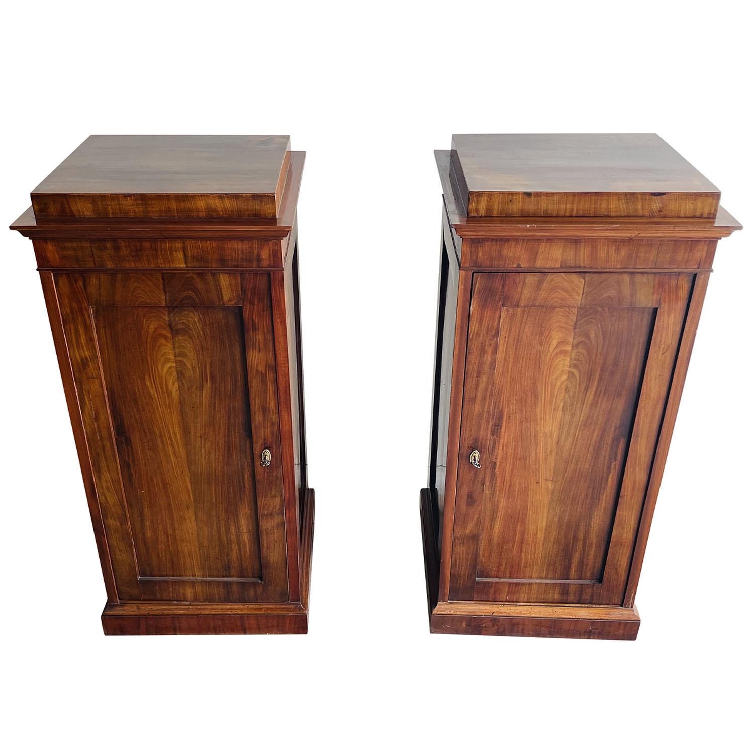 An early 19th Century, antique German Biedermeier pair of podiums made of hand crafted shellac polished, partly veneered Mahogany, in good condition. Each of the detailed pedestals are composed with two shelving, consisting their original hardware