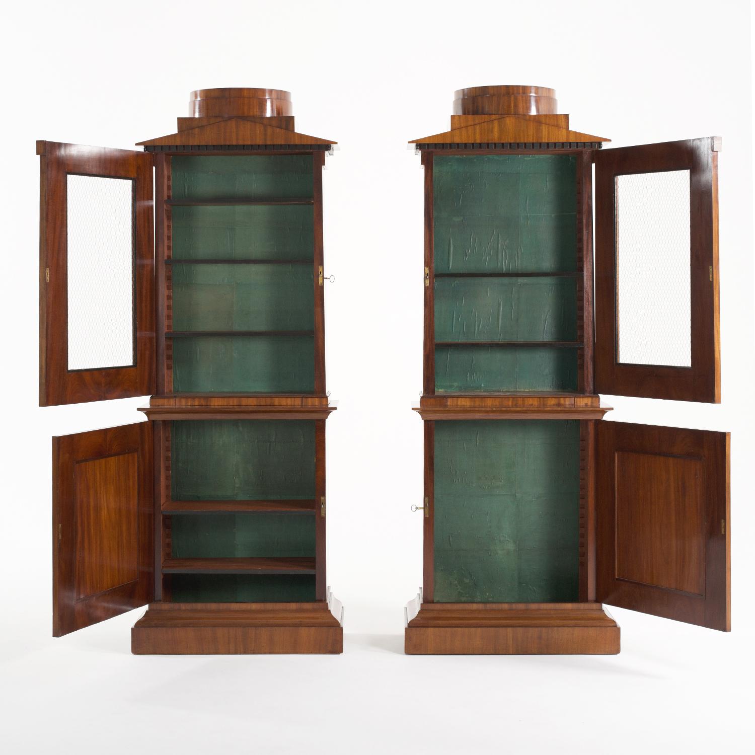 An antique pair of Northern German early Biedermeier bookcases made of shellac polished, partly veneered Mahogany in good condition. The top part of the tall library cabinets are enhanced by a hand crafted cornice, composed with two open doors which