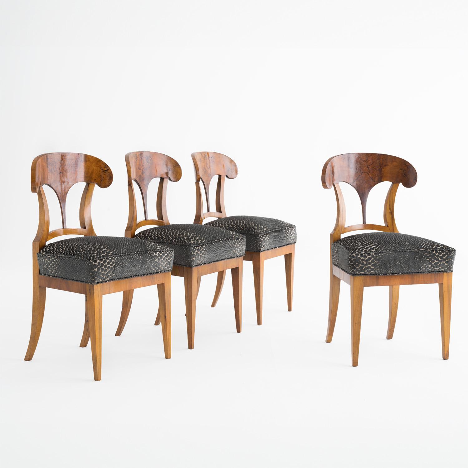 An early 19th Century, antique set of four German dining room chairs made of hand crafted shellac polished, partly veneered Cherrywood, in good condition. The detailed Shovel side chairs have a slightly curved, sculptural backrest, standing on four