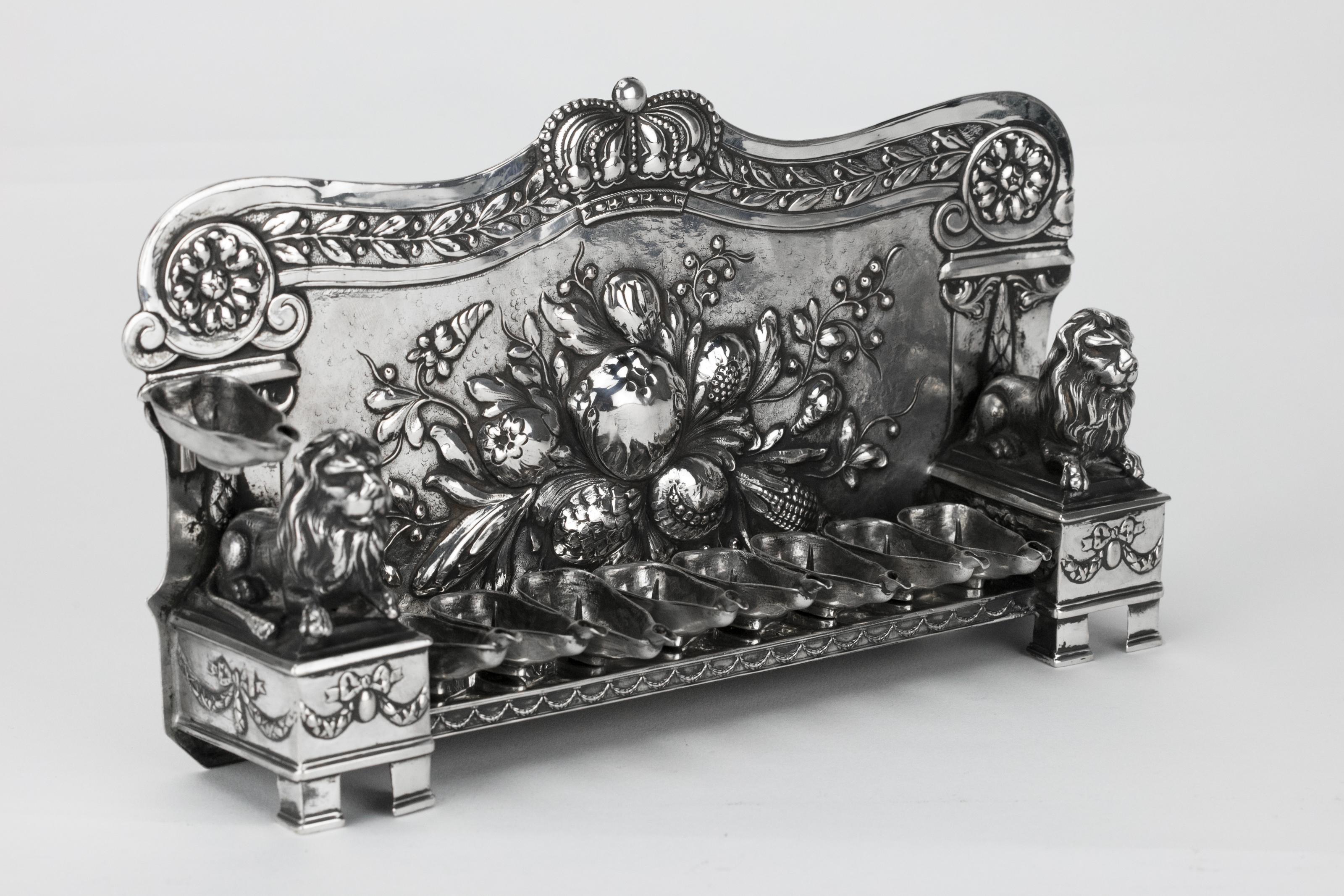 19th century silver Hanukkah Lamp Menorah, Germany, circa 1880. 
The backplate is embossed and chased with a cluster of fruits and flowers surmounted by a crown and flanked by pillars. Pillars fronted by a pair of sculpted Judah lions, seating on