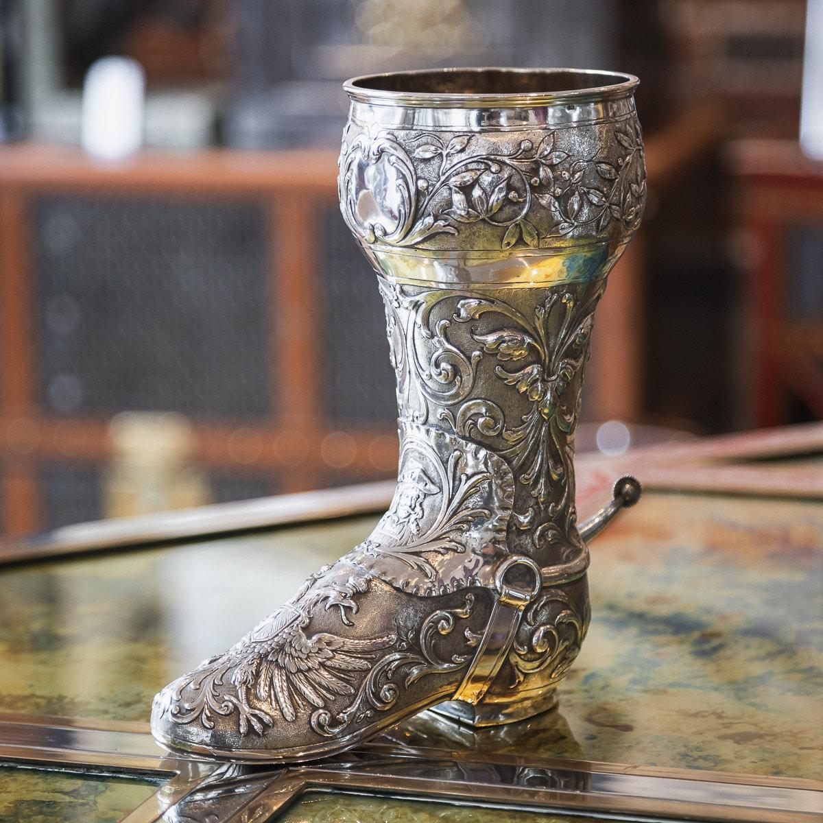Antique late-19th century German very rare solid silver novelty boot shaped drinking vessel, very decorative and ornate in design, chased with scrolling foliage, a double headed eagle, realistically modelled strap and buckle and the heal applied
