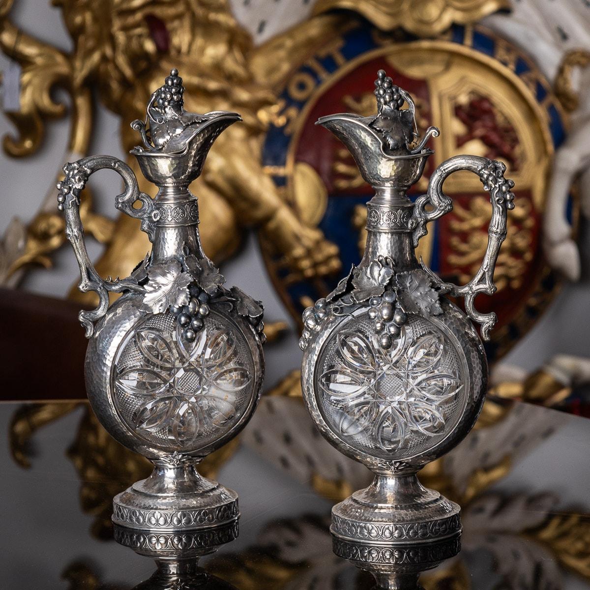 19th century pair of German silver mounted on glass wine jugs, magnificent and highly decorative, the clear-glass body beautifully cut, the silver mount applied with foliage and grapes, the handle is realistically modelled as grapevine, the body