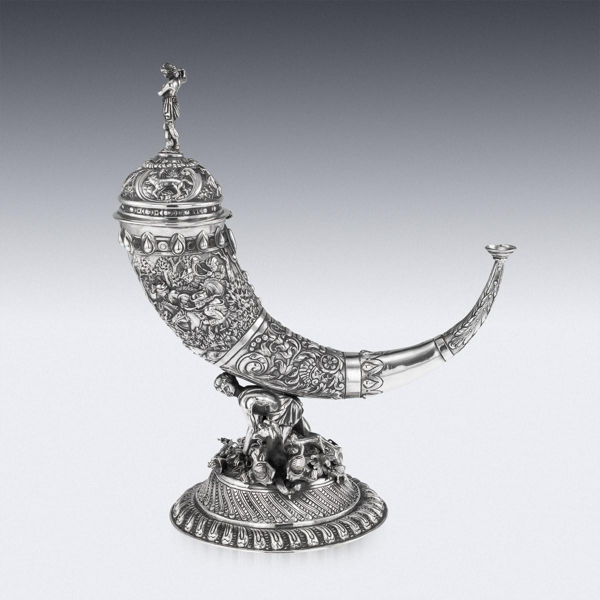 Antique late-19th century German solid silver lidded drinking cup, shaped as a hunting horn. Embossed throughout with hunting scenes, depicting hunters riding on horseback through a dense forest, chasing a stag. The horn supported by a hunter with