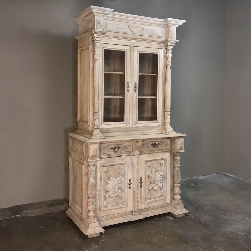 19th century German stripped oak bookcase with lamb of god features stately neoclassical architecture, bold molding, tapered and fluted columns above and below, and the lamb of god in mirror images carved in full relief on the lower doors. Upper