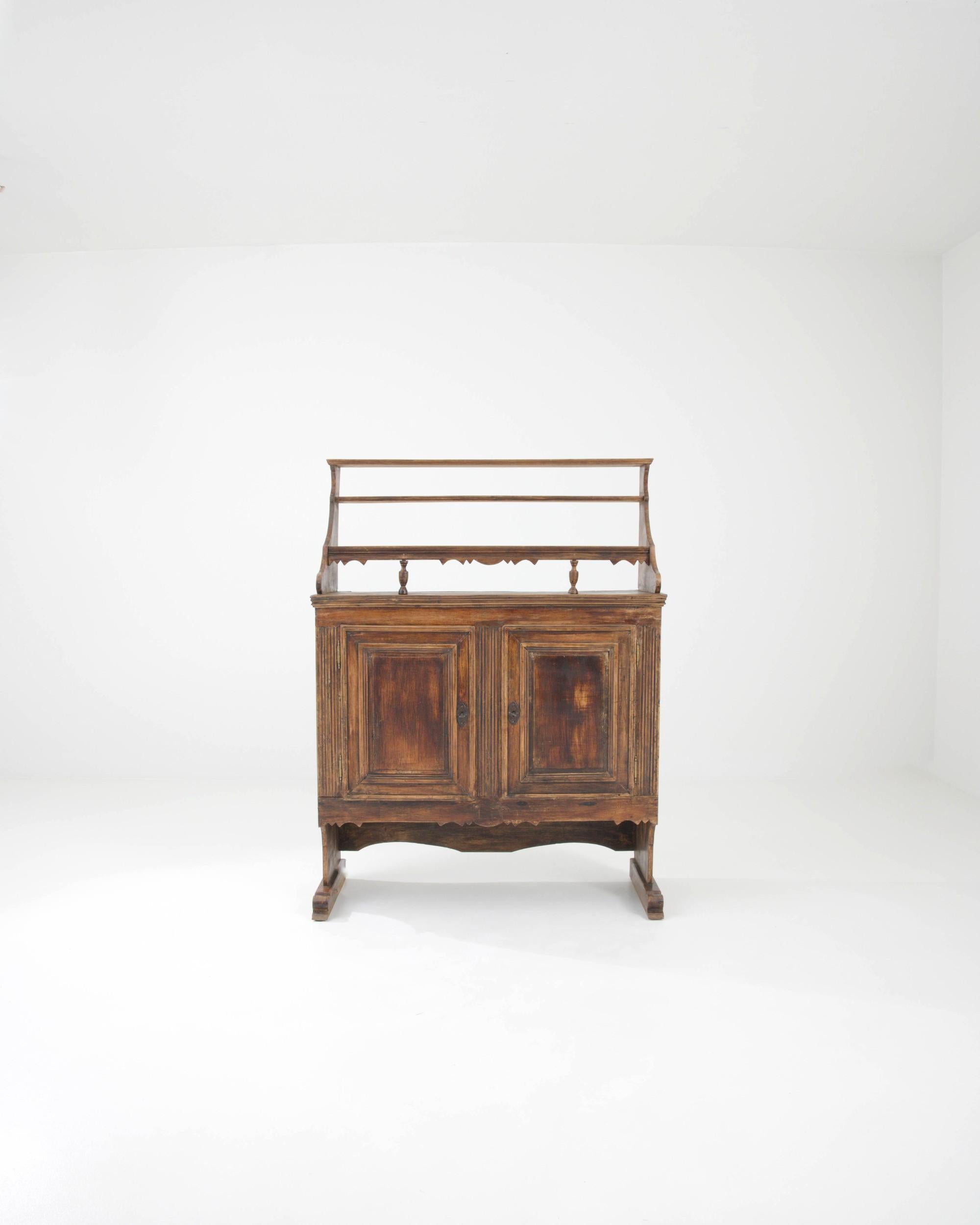 With its handsome design and rich original patina, this antique wooden cupboard offers a distinguished period piece. Hand-built in Germany in the 1800s, the composition combines generous storage space with a set of upper display shelves. Contoured