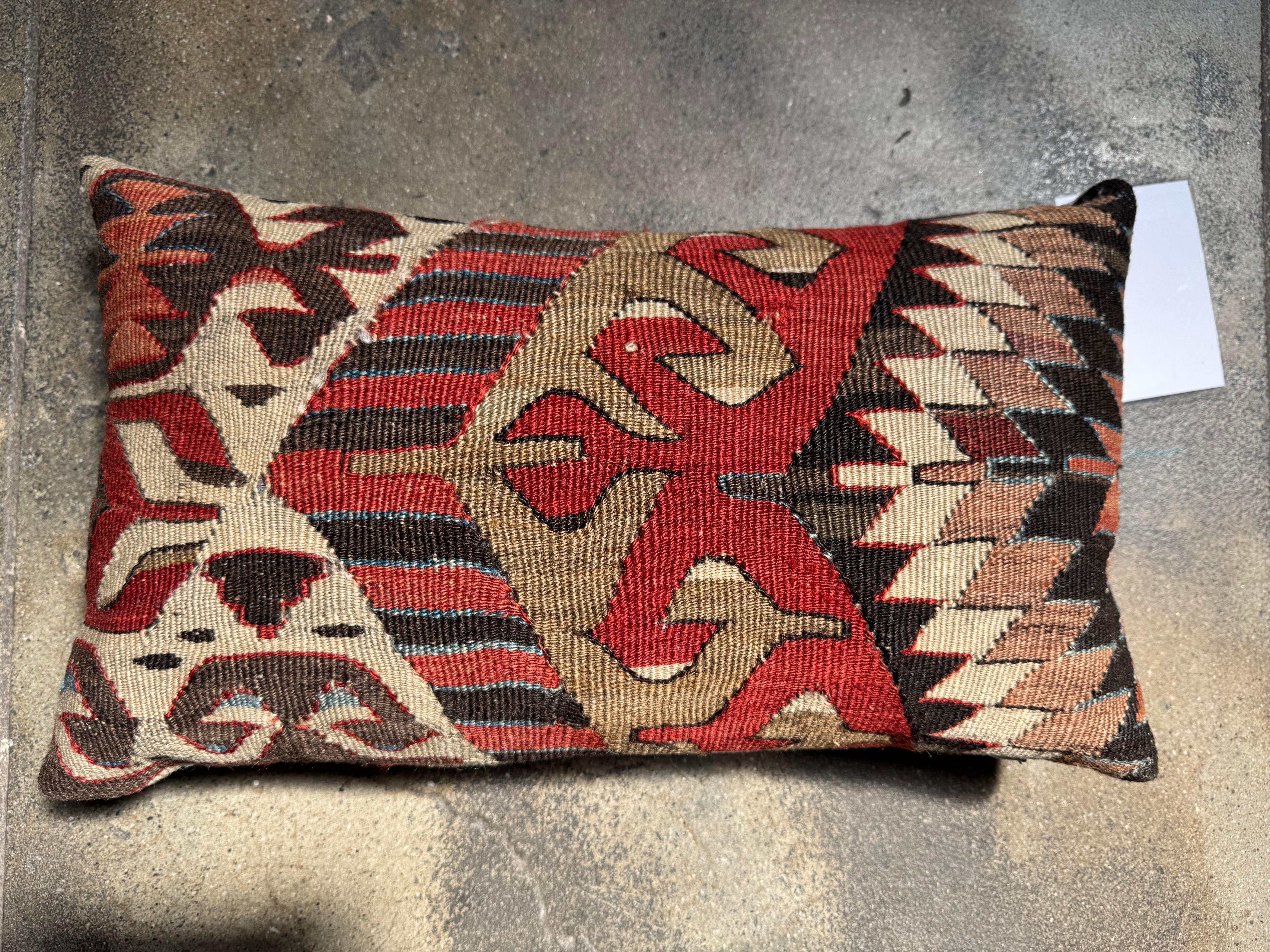 Infused with rich history and artisanal craftsmanship, this 19th Century Ghashghai Kilim lumbar pillow brings timeless tribal beauty into any interior. Handwoven from wool with intricate geometric and symbolic patterns in earthy reds, browns, and