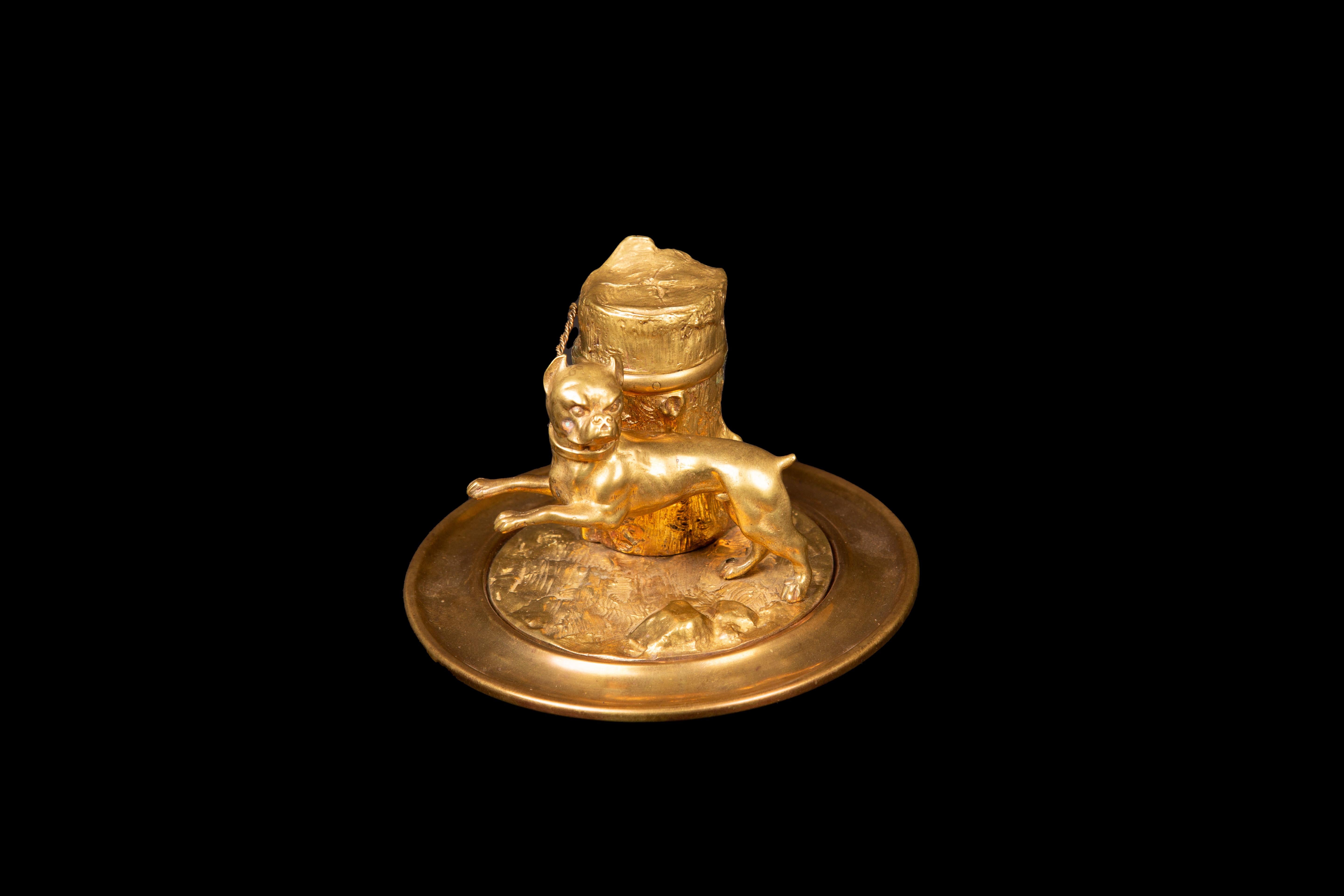 This 19th-century gilded inkwell is a captivating piece of artistry, masterfully crafted to depict a charming bulldog tethered to a rustic tree stump. With intricate details and a touch of opulence in its gilded finish, this inkwell not only serves