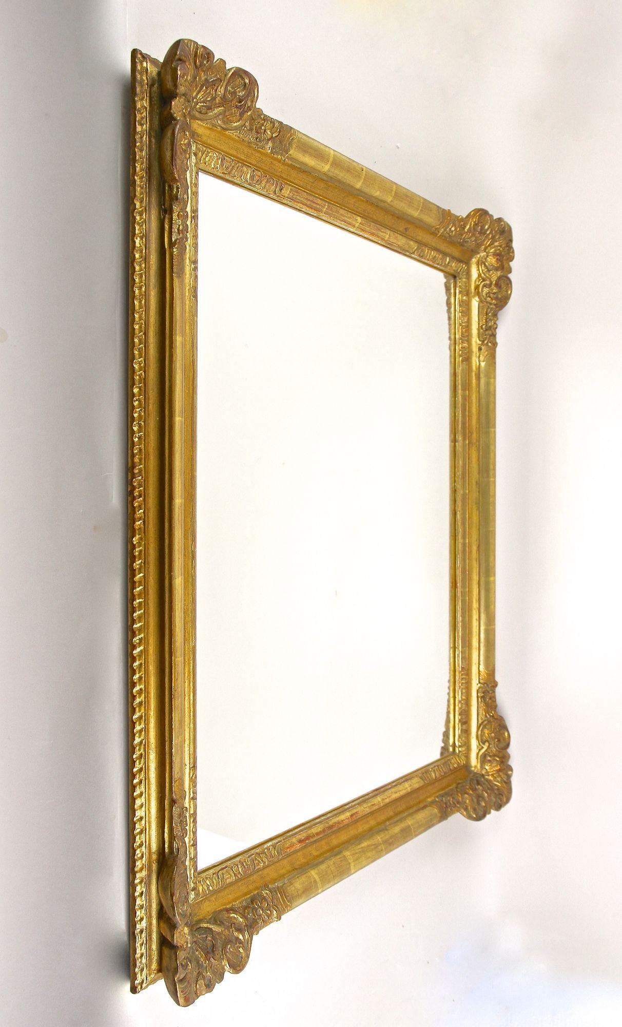 Noble miroir mural doré du 19ème siècle de la célèbre période Biedermeier en Autriche. Ce magnifique miroir mural ancien a été sculpté à la main vers 1850 et impressionne par son cadre détaillé montrant des motifs floraux créés avec art, avec des