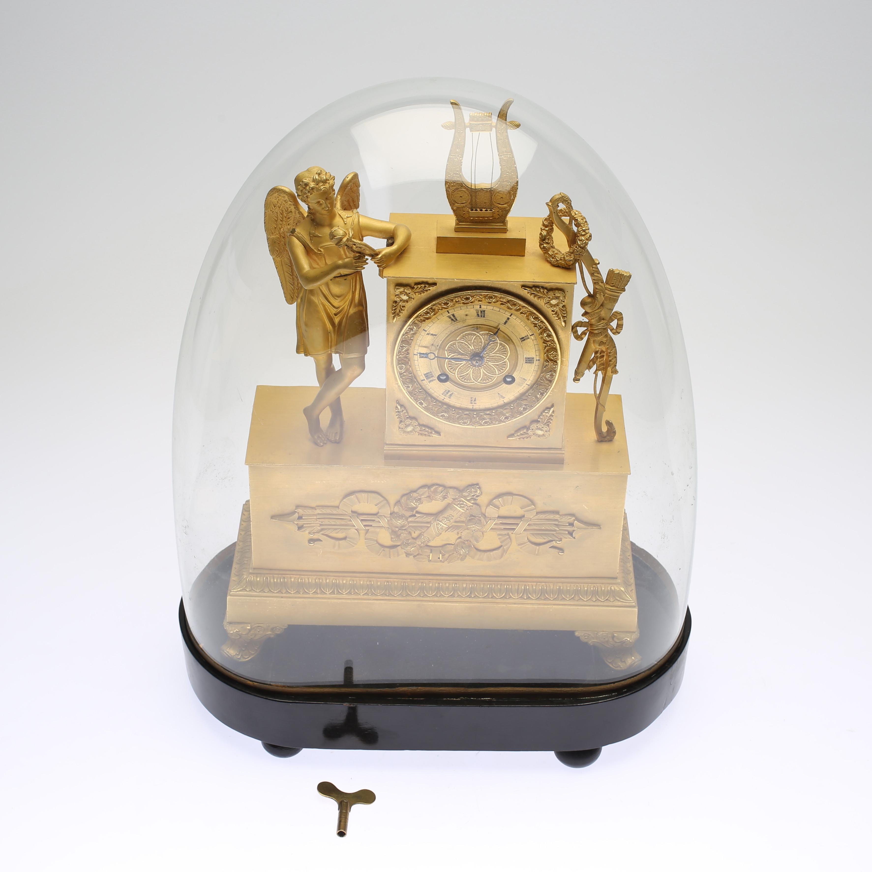 Early 19th century gilt brass mantle clock with the glass hood. Decor of foliage, arrows, and bow. Crowned by an angel with lyre. The glas dome has protected it beautifully and it is in beautiful condition for its age.
