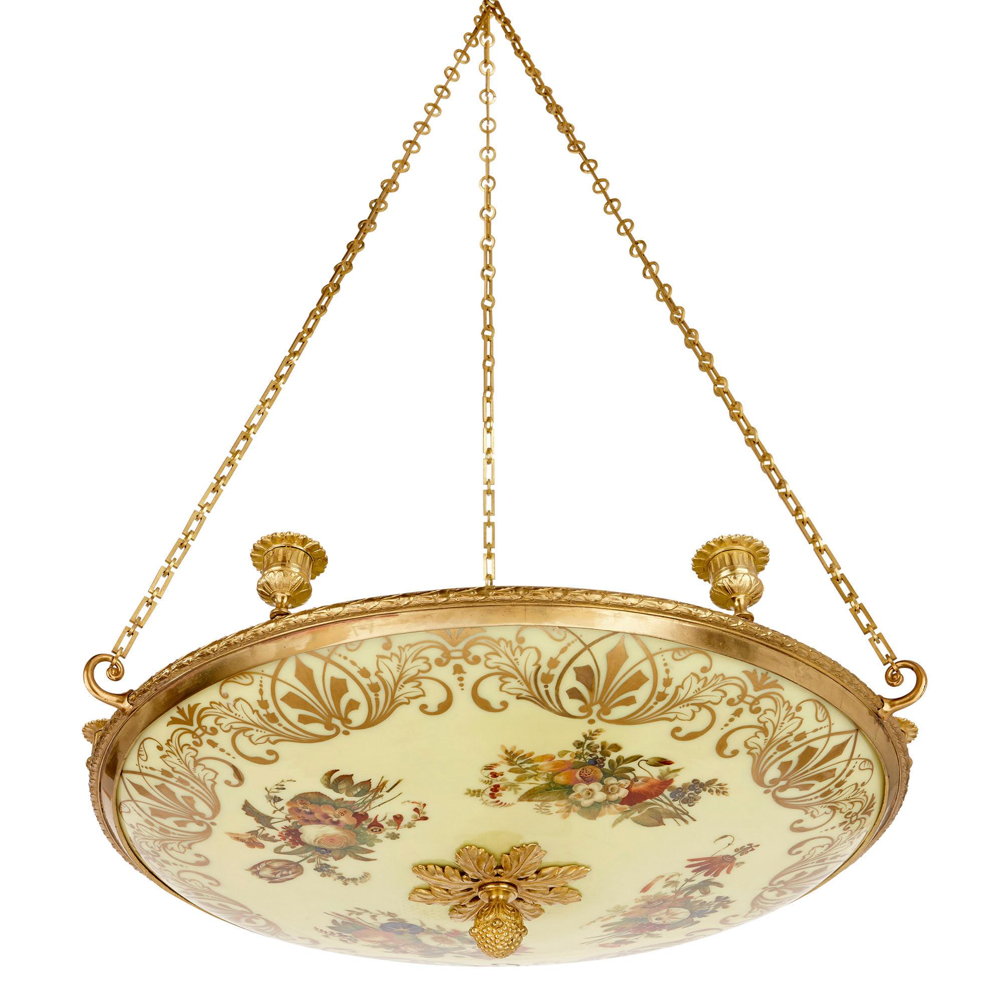 This shallow bowl chandelier is set within a gilt bronze (ormolu) mount, which is designed in the manner of a stylised wreath. The mount supports six candle holders and is suspended from three gilt bronze chains, the links of which take the form of