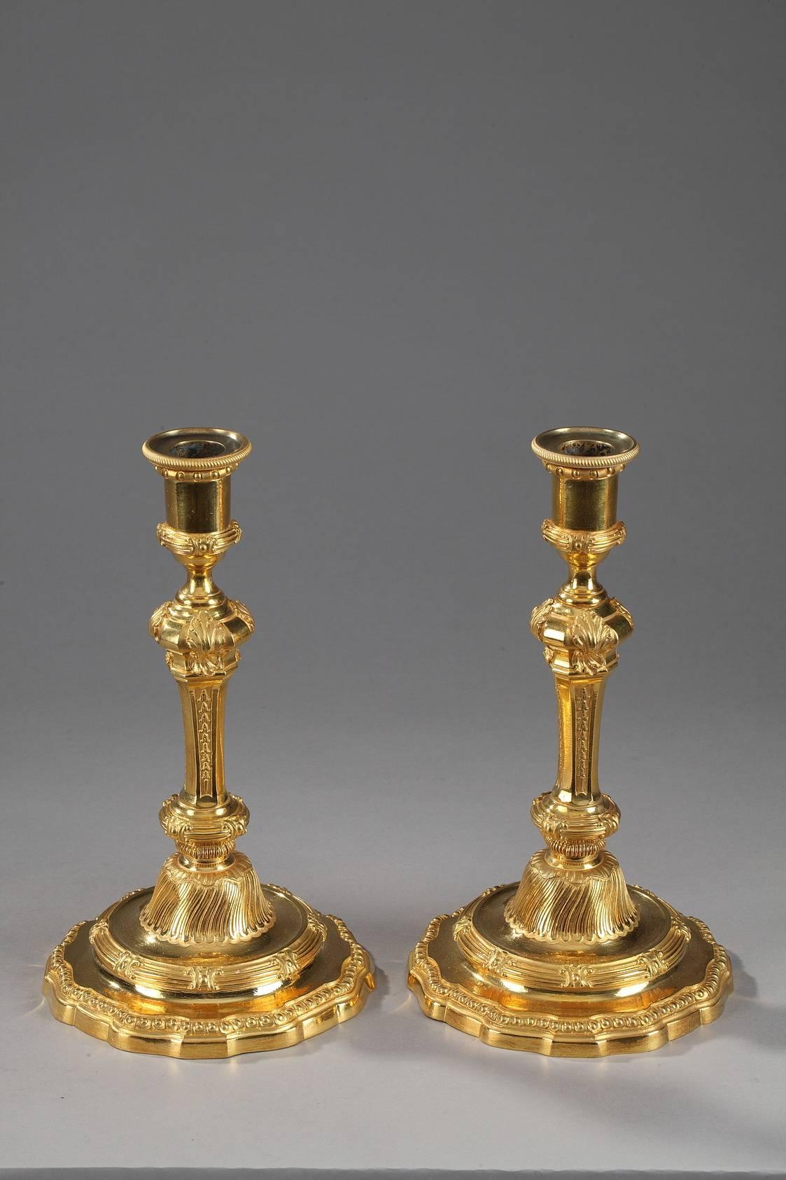 Pair of Ormolu candlesticks with stems embellished with floral patterns topped by intricately sculpted foliage. The socket is decorated with ribbed lines interspaced with ovals. Each candlestick rests on a circular base and is decorated with curved