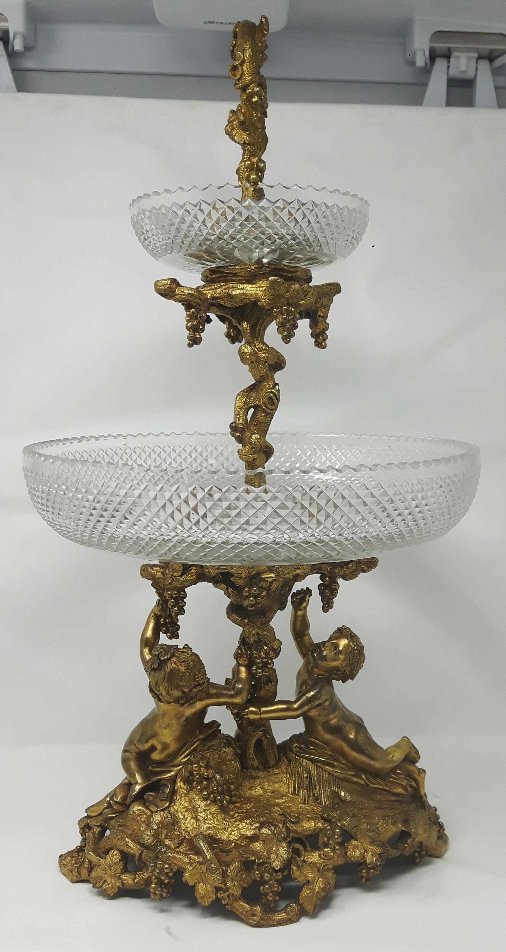Ein Tafelaufsatz aus vergoldeter Bronze, mit zwei scharf geschnittenen Schalen auf einer Fruchtranke, die von zwei Putten auf einem ovalen Sockel getragen wird.